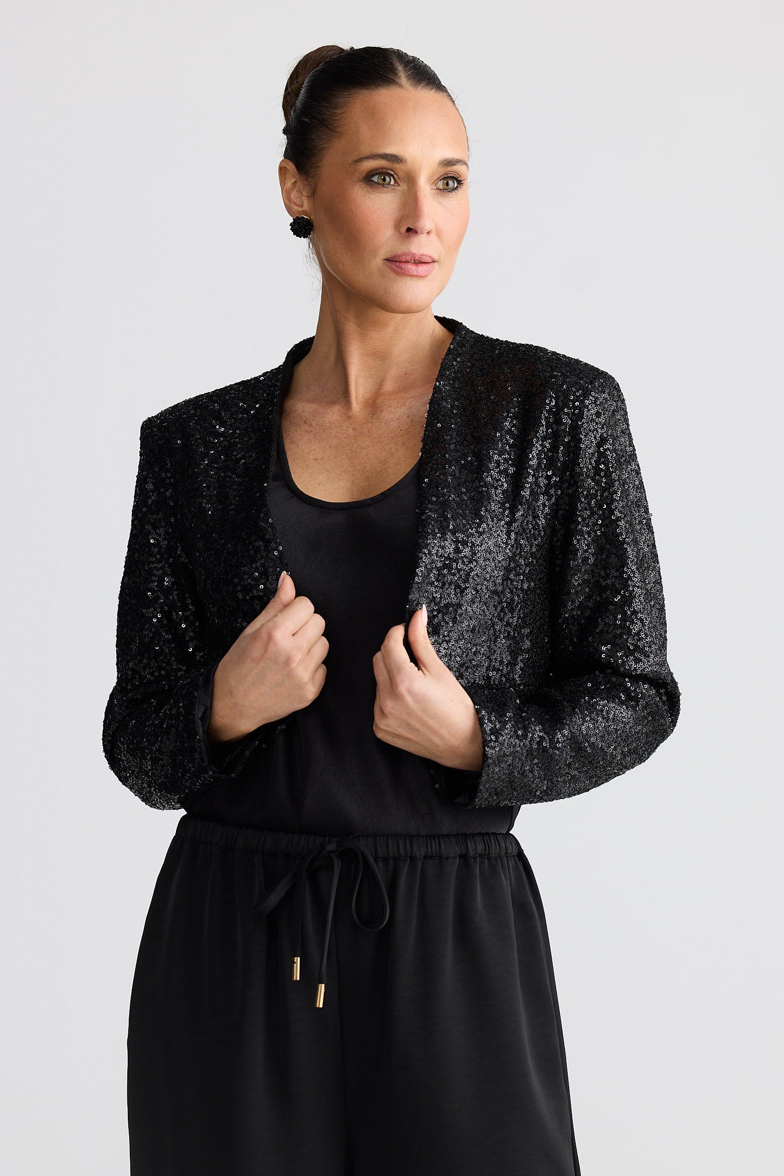 Woman wearing a black sequin jacket over a black outfit on a light gray background