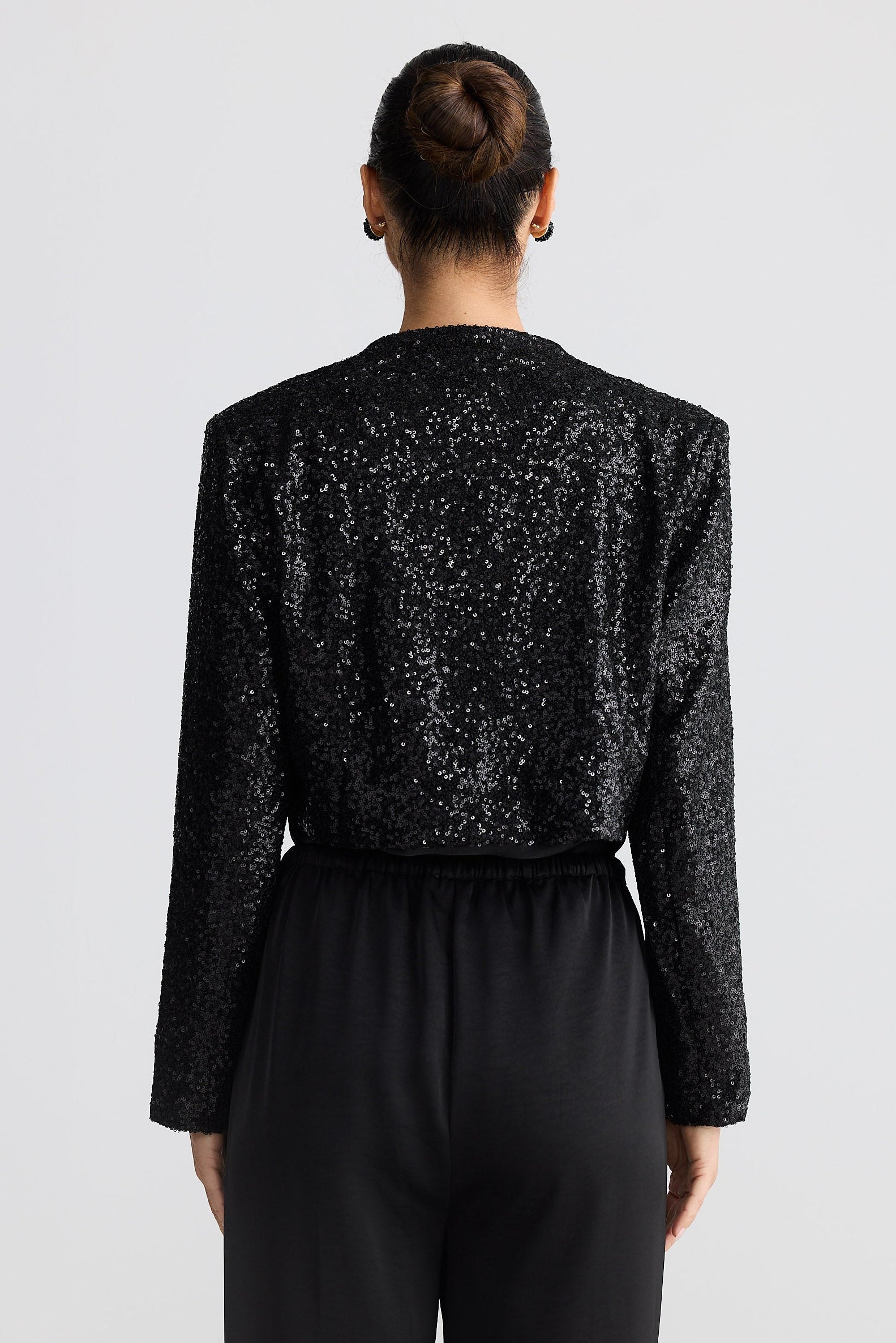 Person wearing a black sequin jacket and black pants on a white background