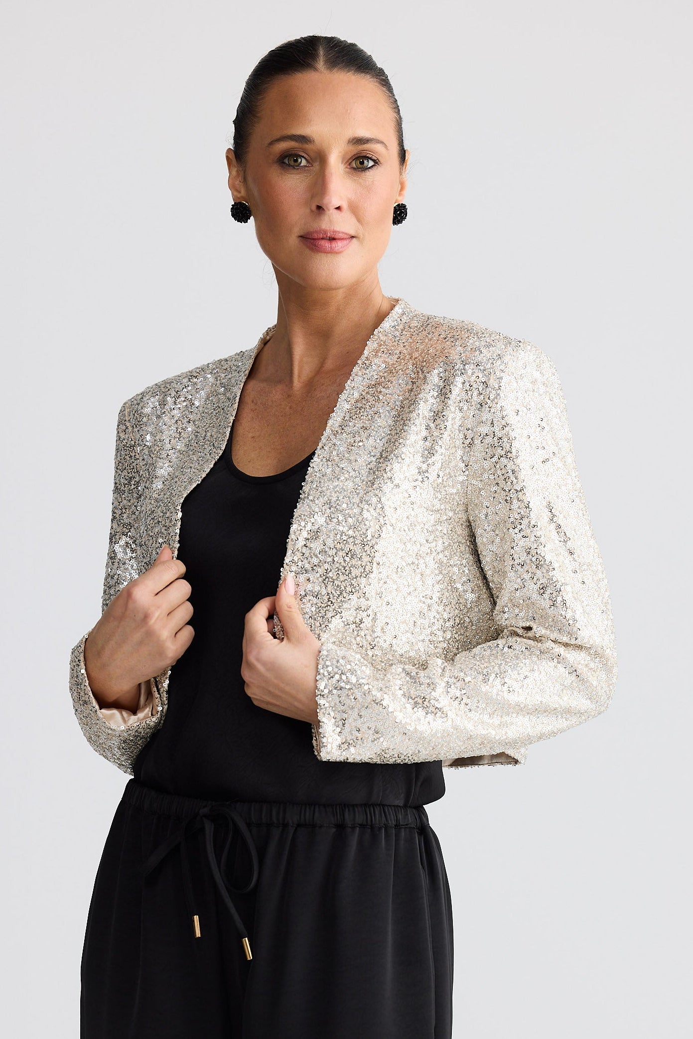 Woman wearing a silver sequin jacket over a black outfit on a white background