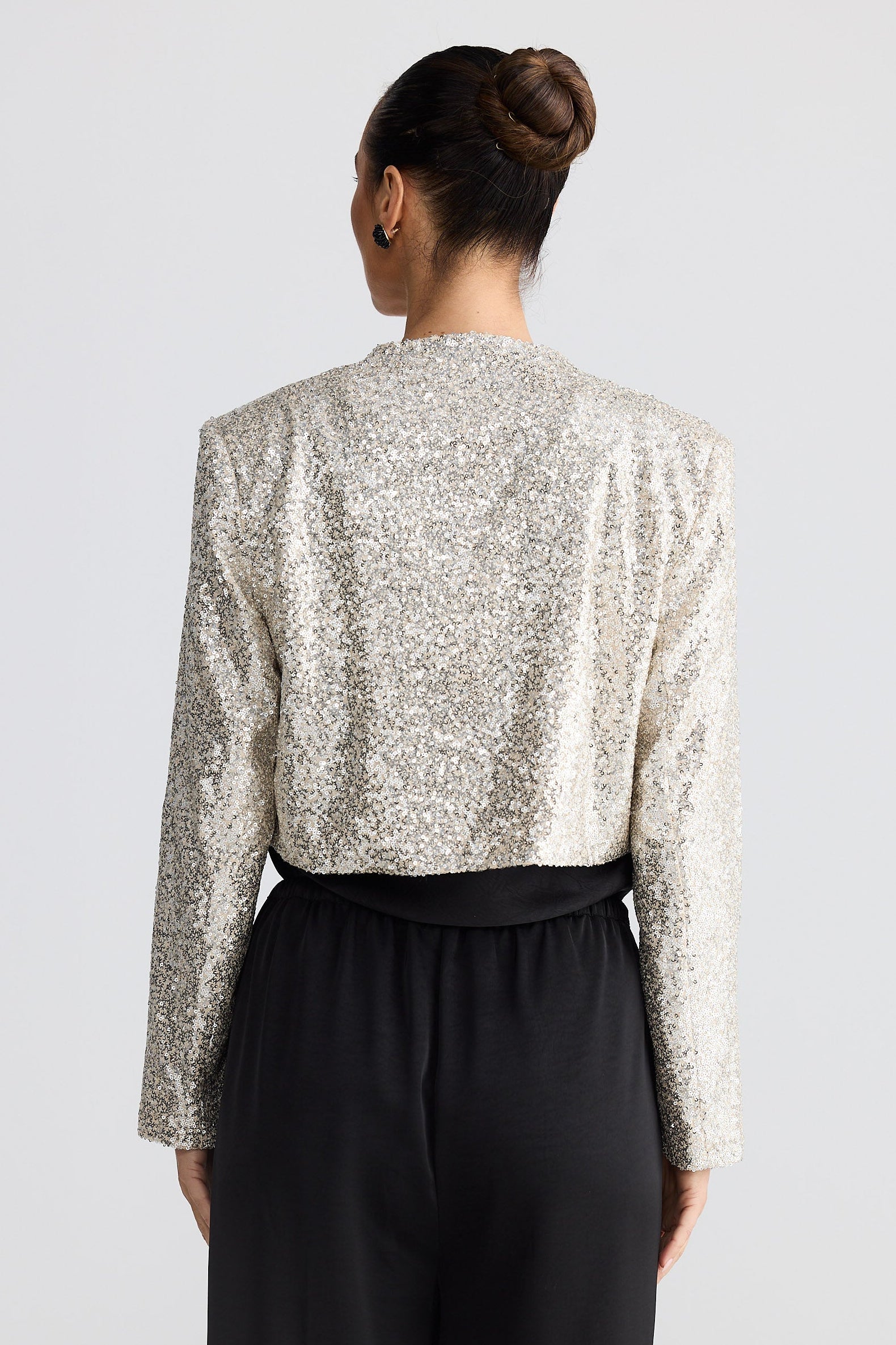 Person wearing a silver sequin jacket and black pants on a light gray background