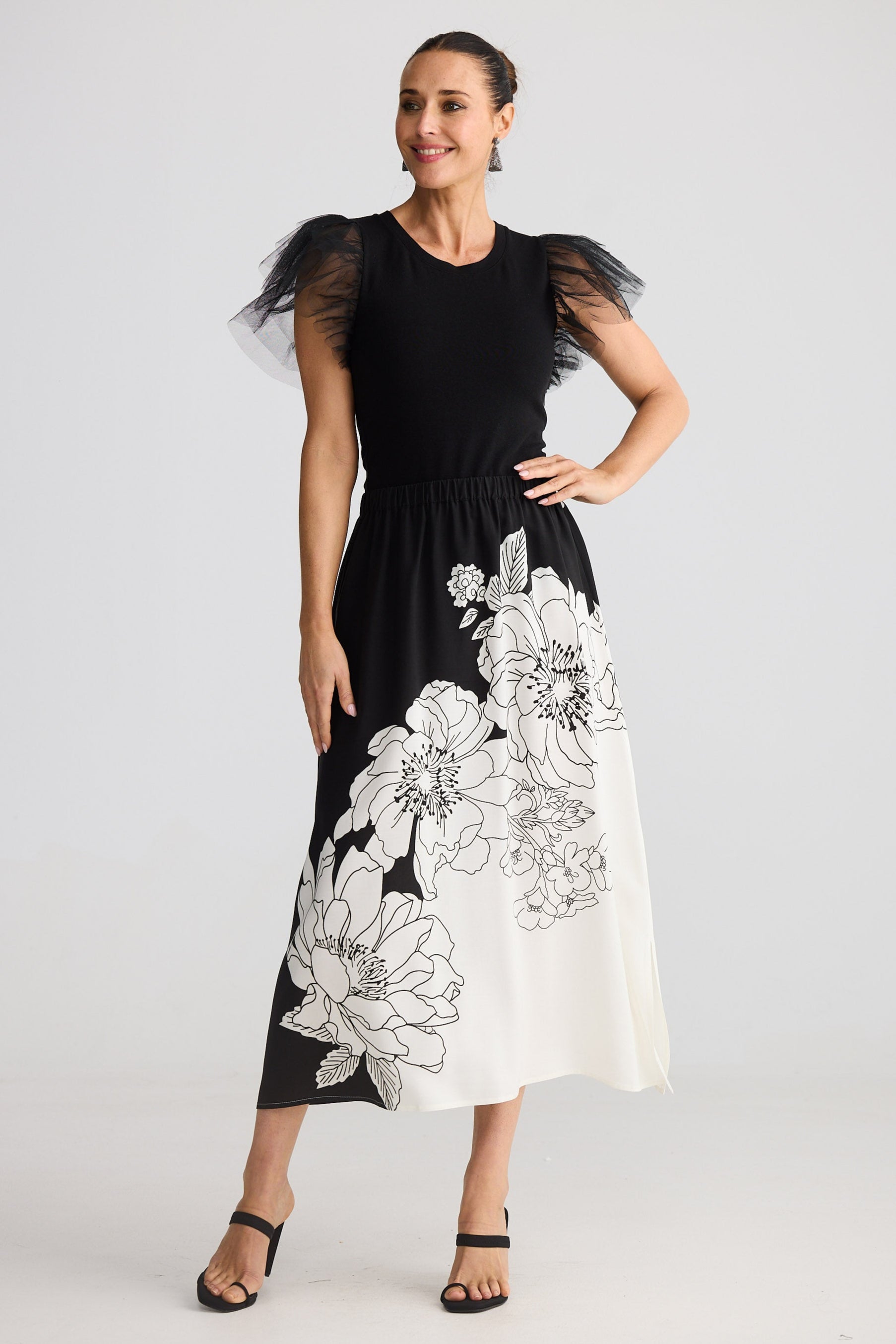 Woman wearing a black dress with white floral patterns on a plain background