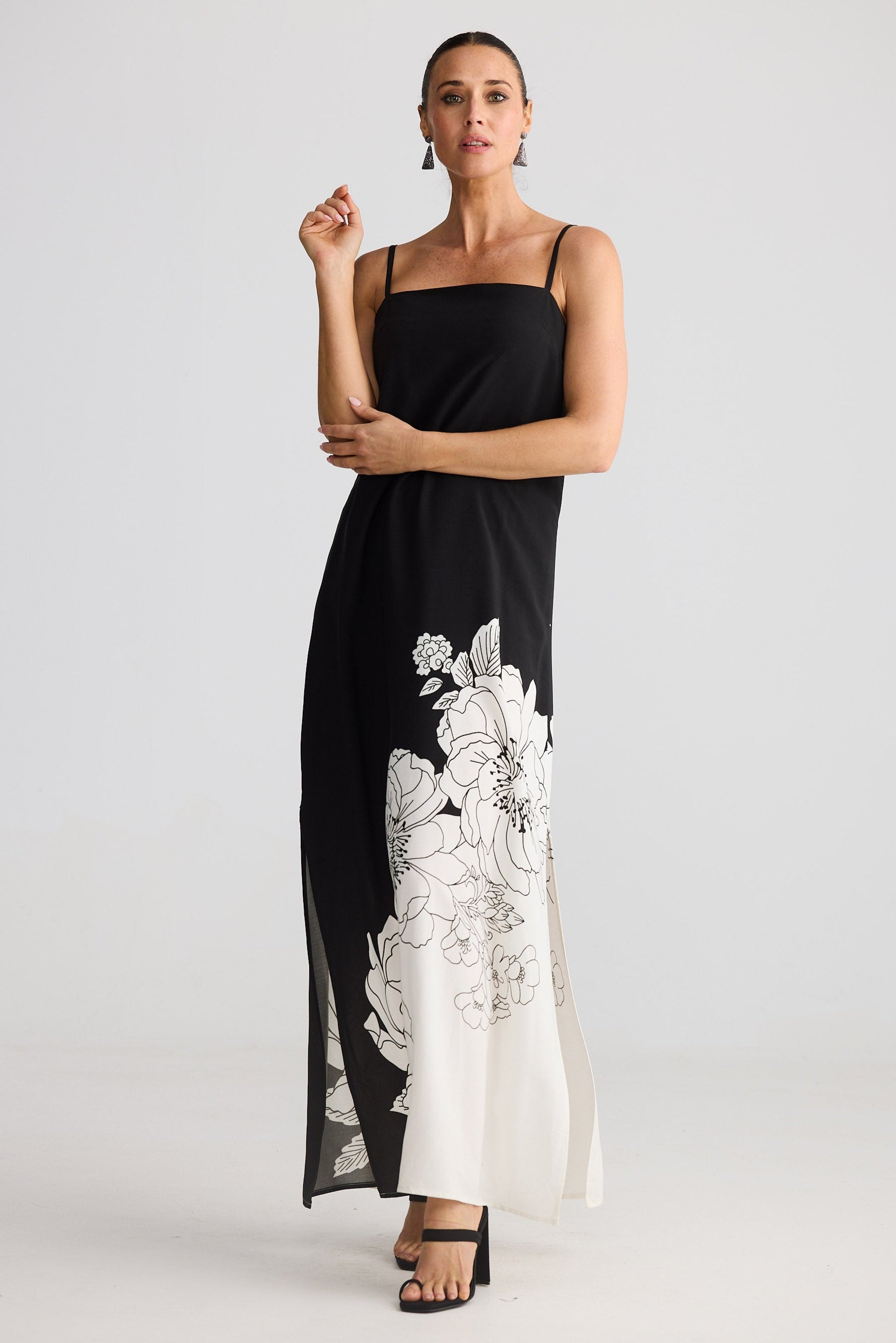 Woman wearing a black dress with white floral embroidery on a plain background