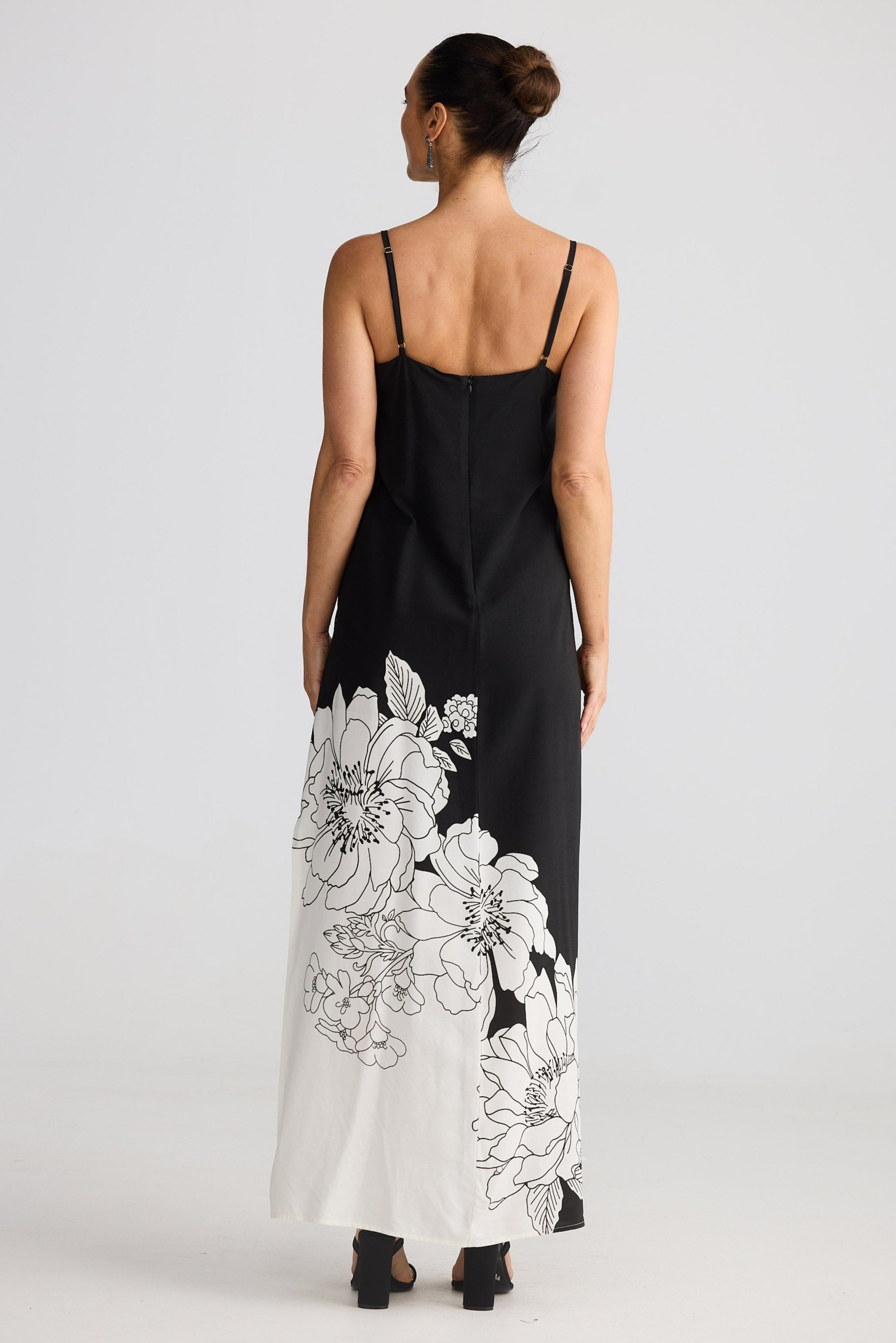 Woman wearing a black slip dress with white floral patterns on a plain background