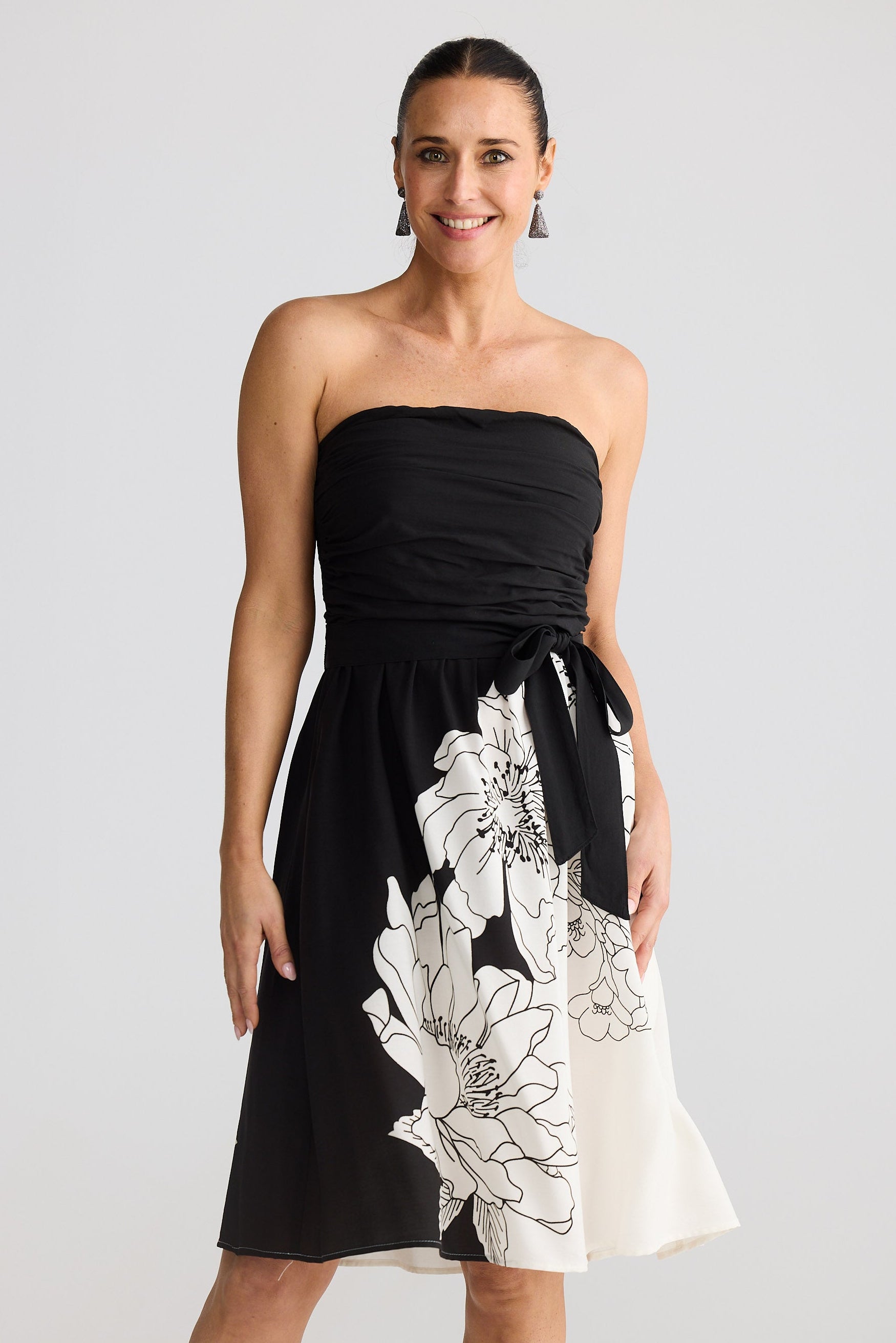 Woman wearing a black strapless dress with white floral patterns on a plain background