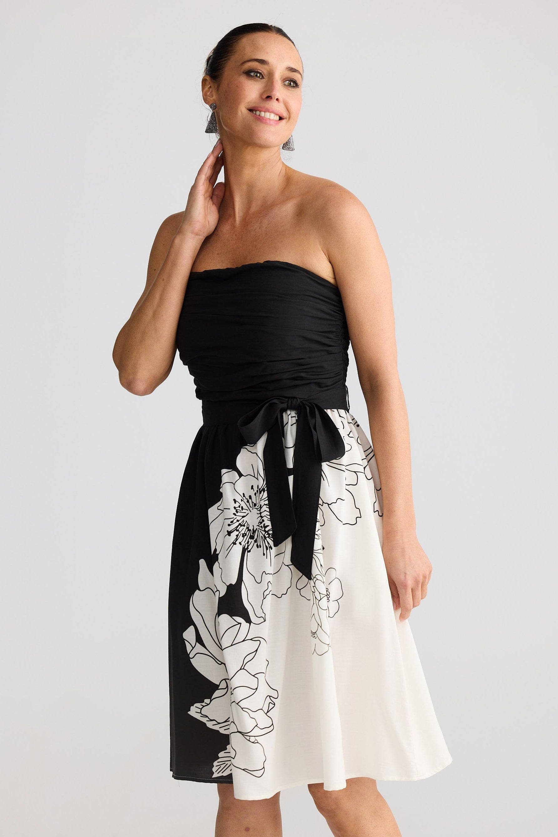 Woman wearing a black and white strapless dress with floral design on a plain background