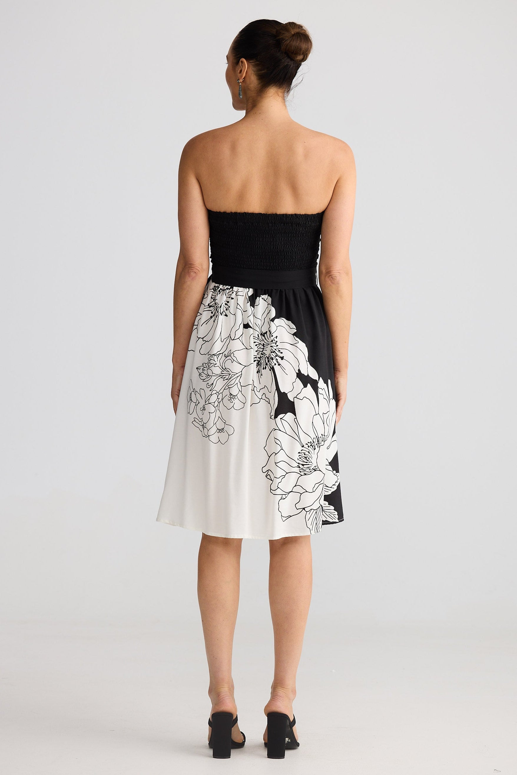 Woman wearing a black strapless dress with white floral patterns on a plain background