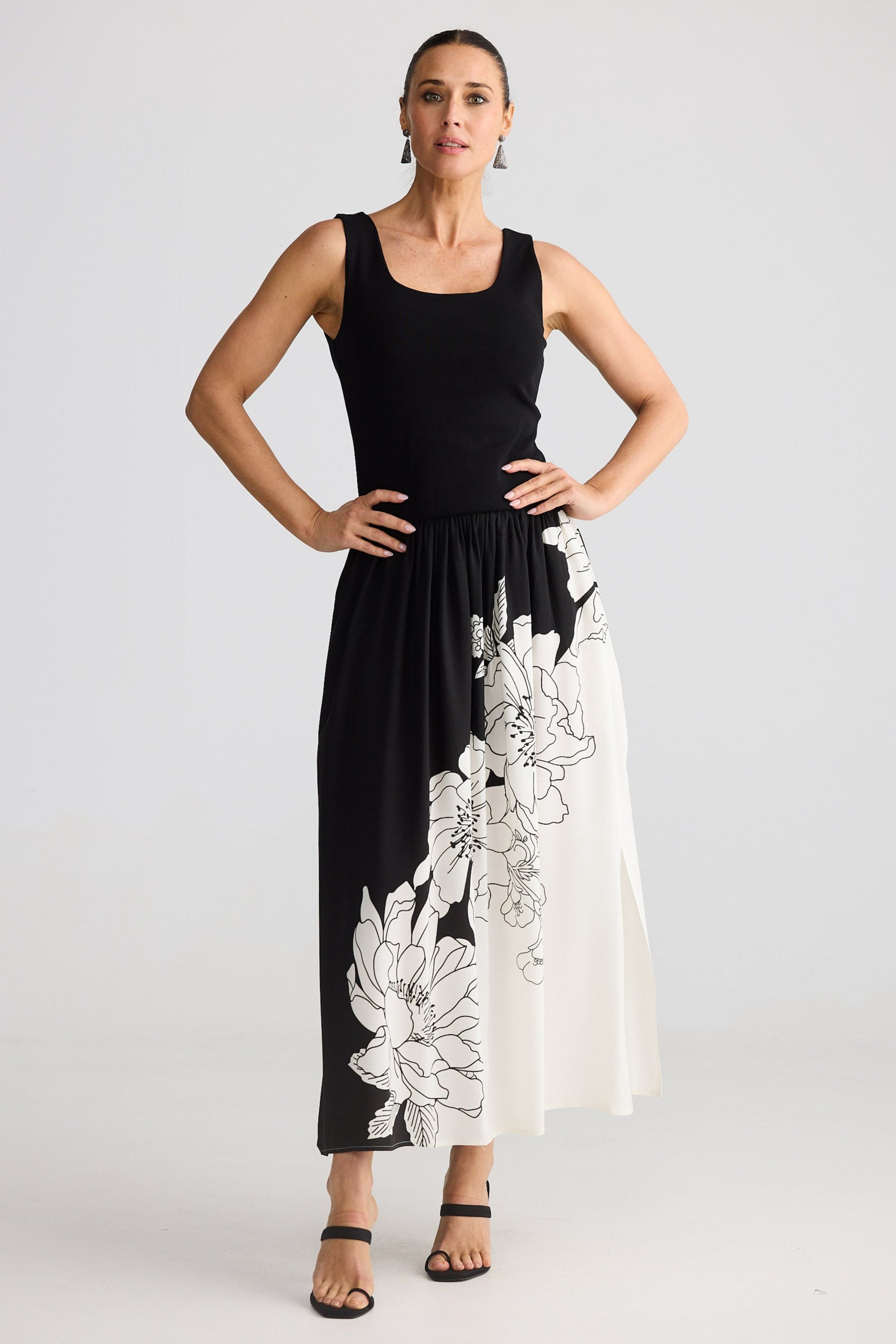Woman wearing a black sleeveless top and long black and white floral skirt on a light gray background