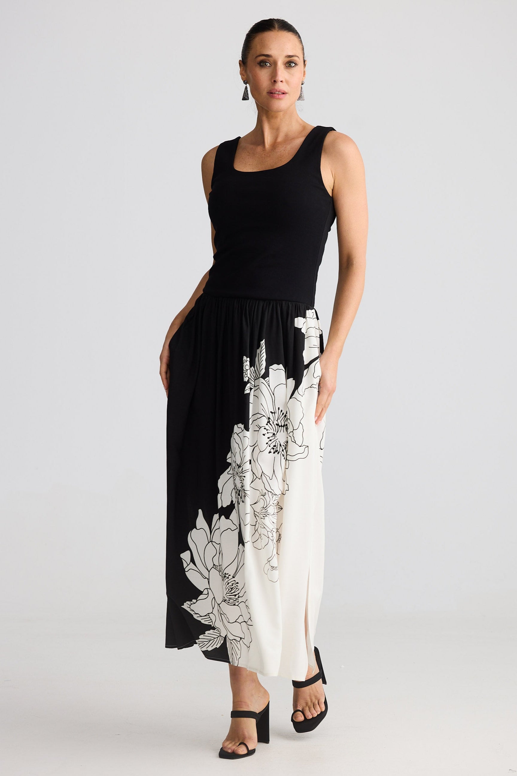 Woman wearing a black sleeveless dress with white floral patterns on a plain background