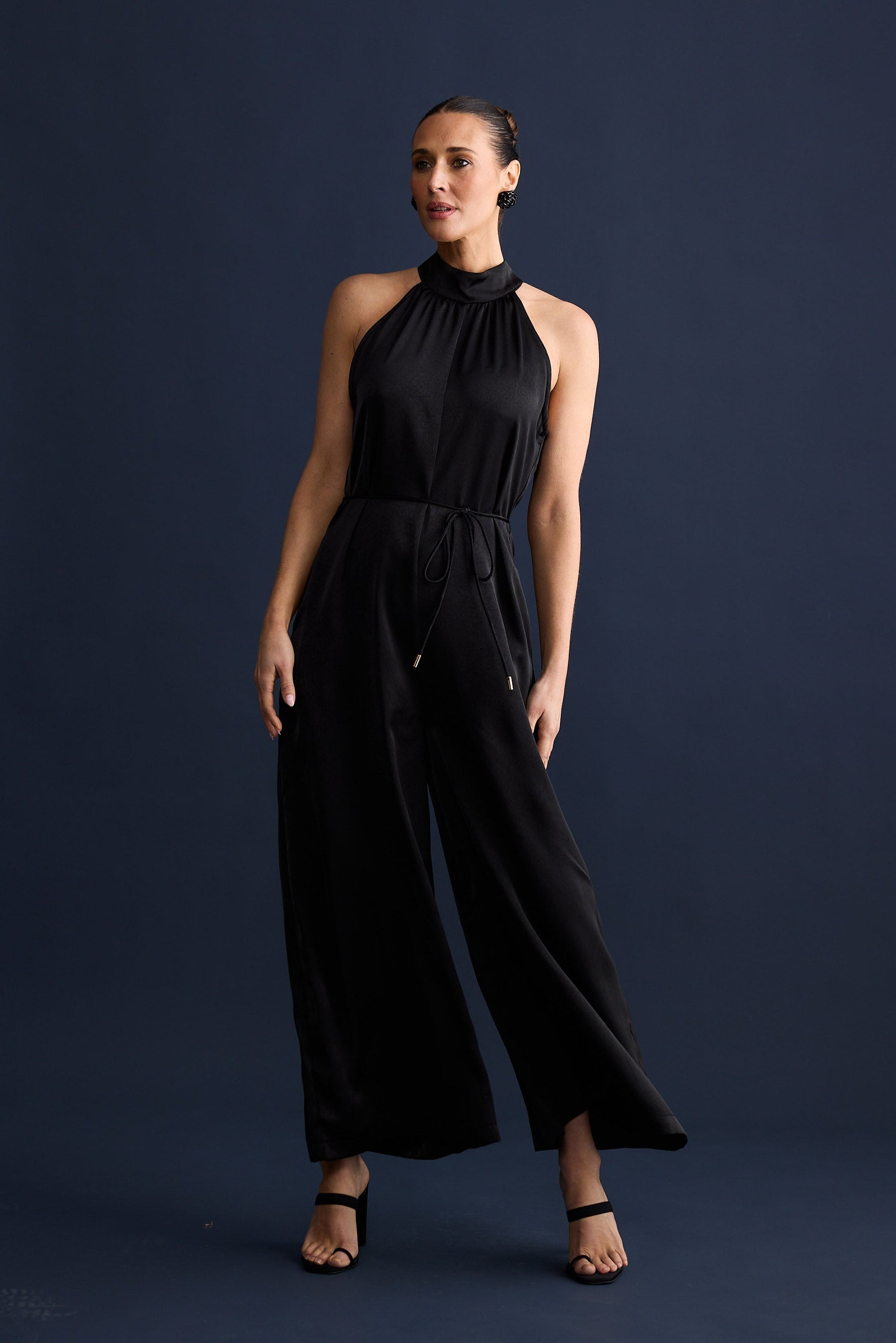Woman wearing a black jumpsuit against a dark blue background