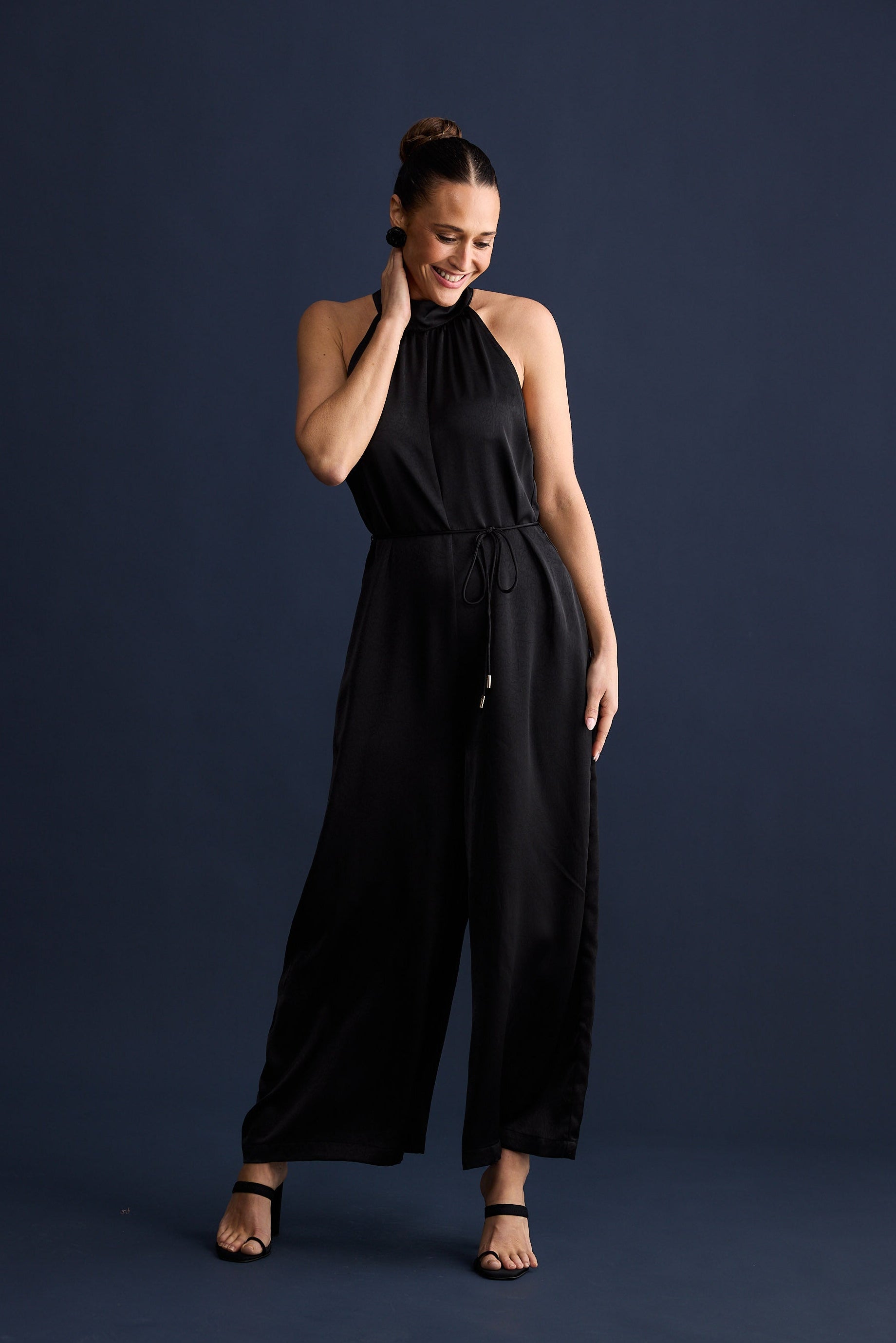Woman wearing a black jumpsuit against a dark blue background
