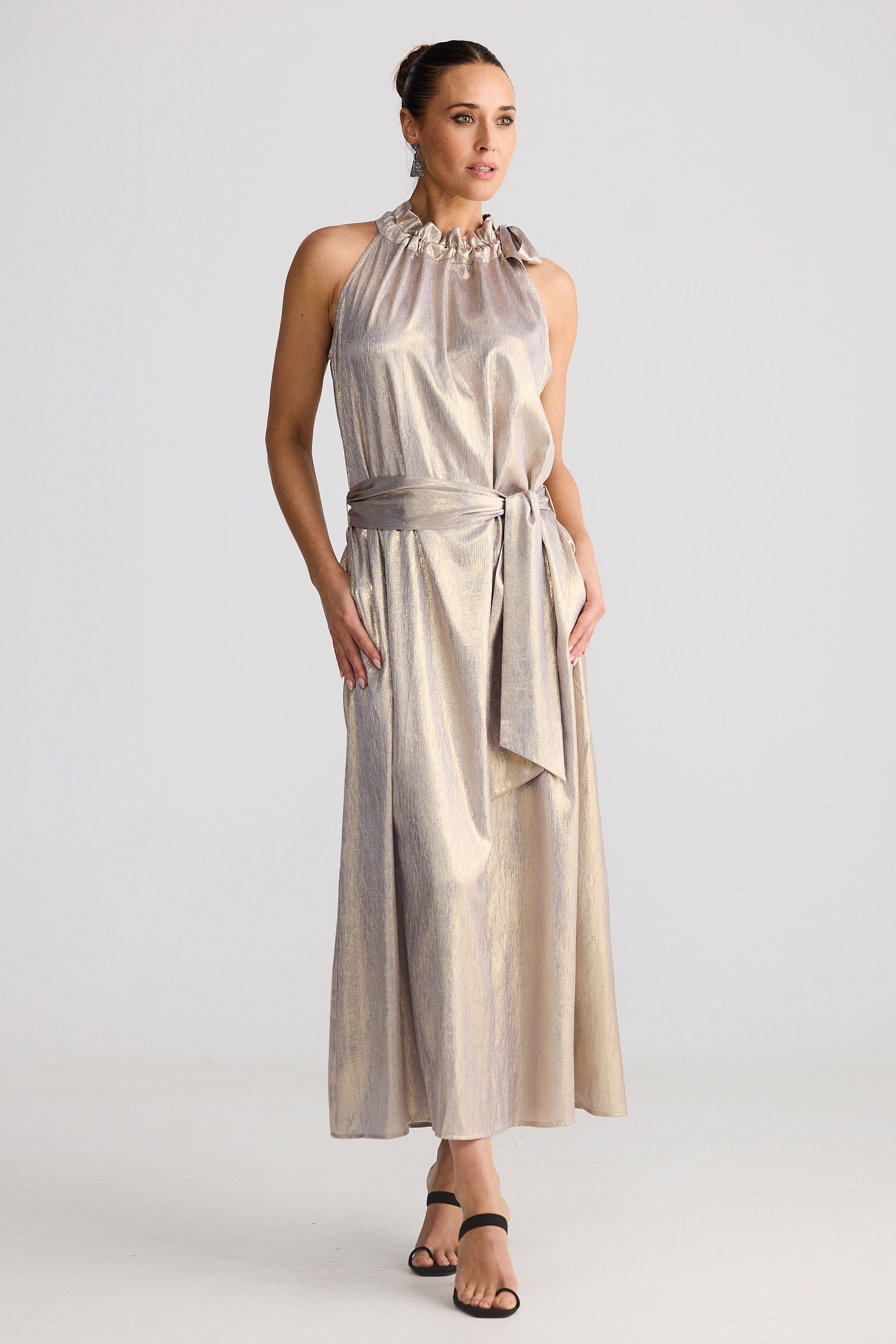 Woman wearing a metallic halter neck dress with a belt on a white background