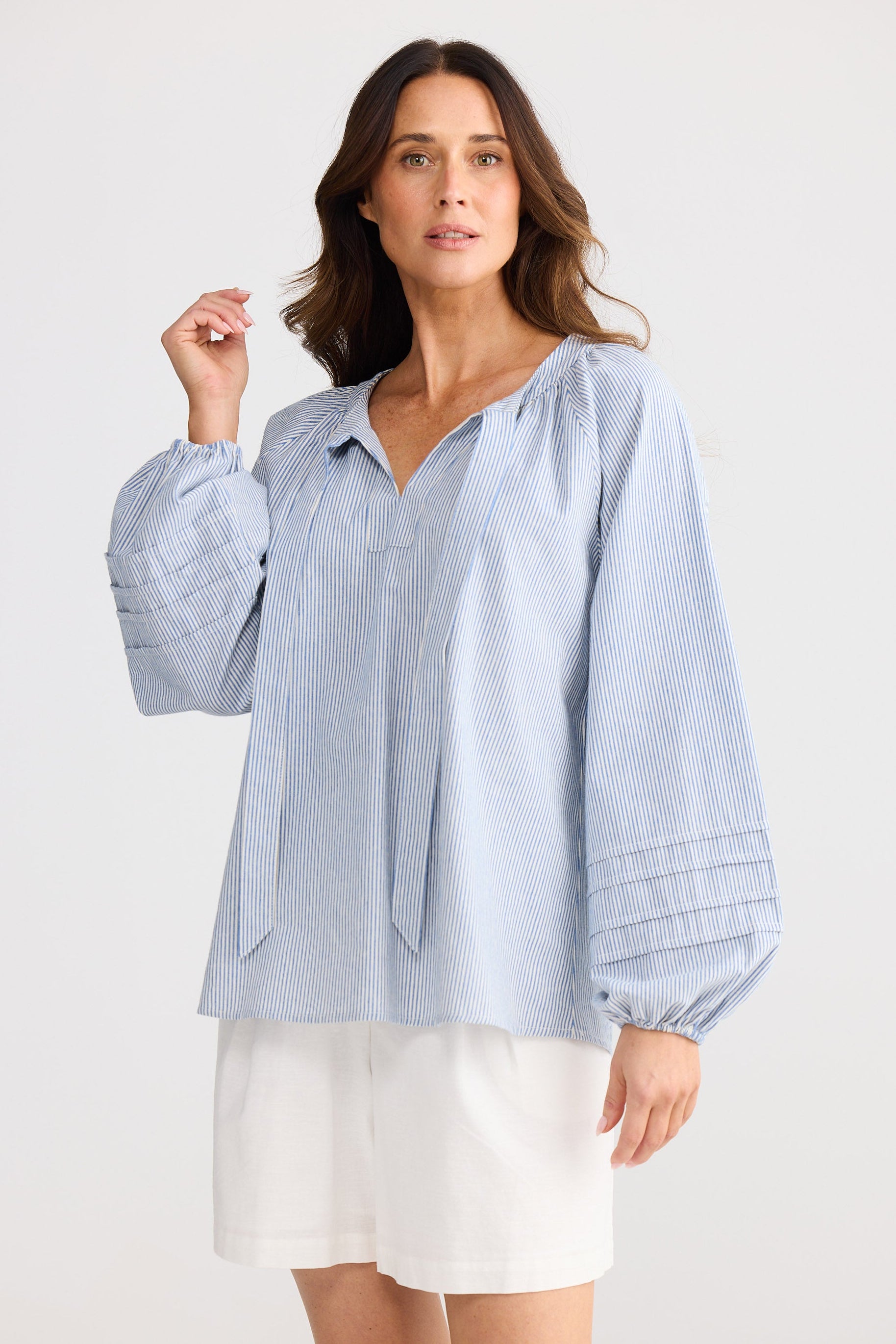 Woman wearing a light blue striped shirt and white shorts on a white background