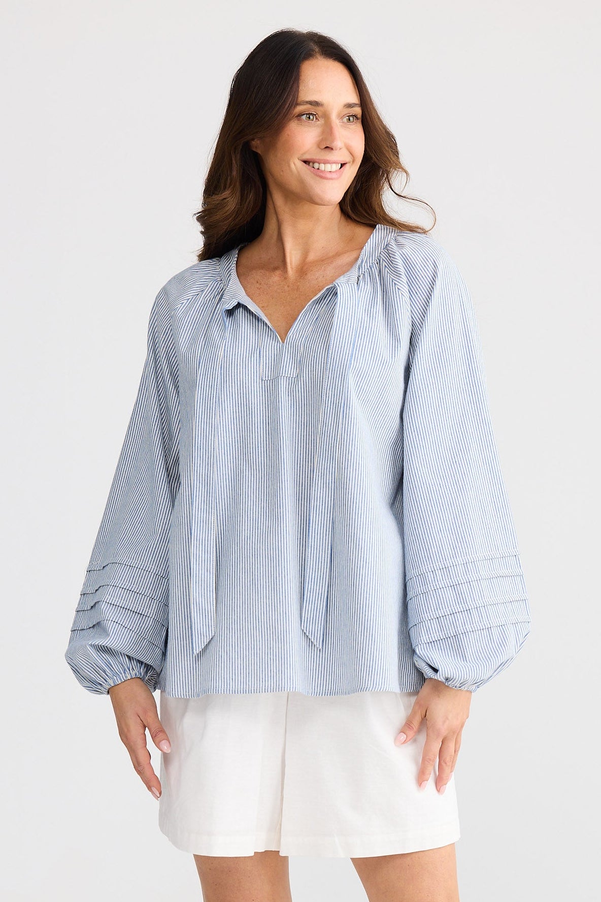 Woman wearing a light blue striped shirt and white shorts on a plain background