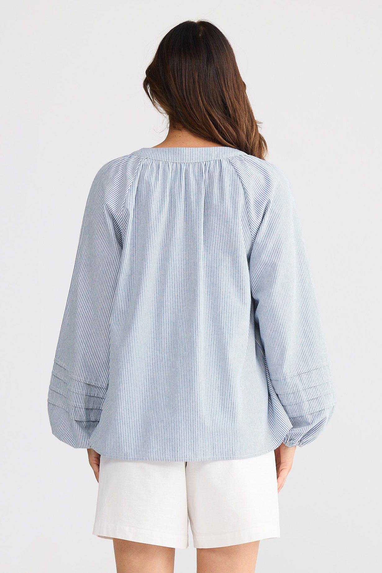 Woman wearing a light blue blouse and white shorts on a plain background