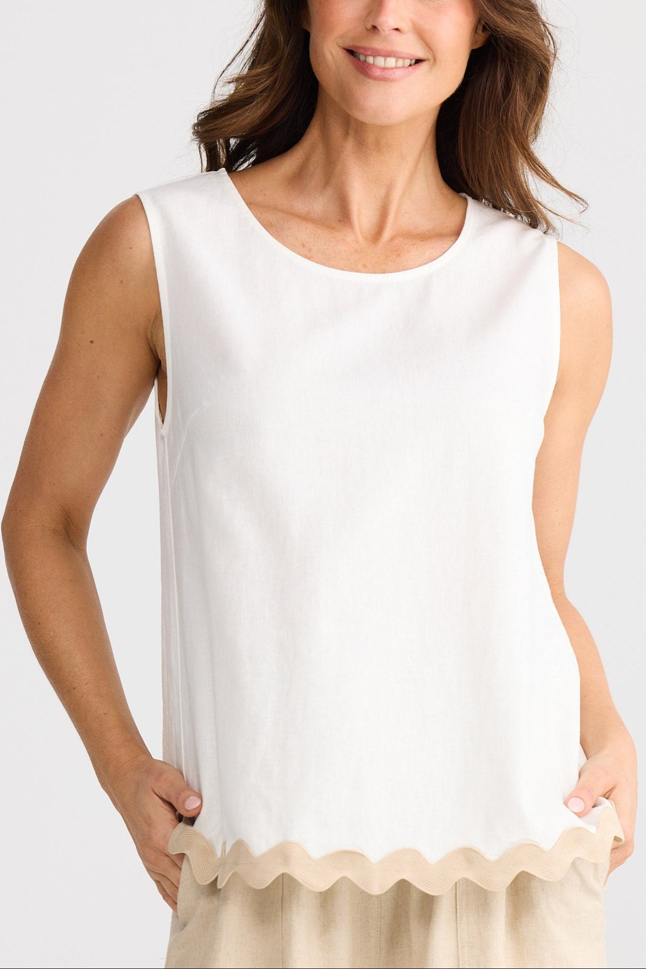 Woman wearing a white sleeveless top and beige shorts on a plain background
