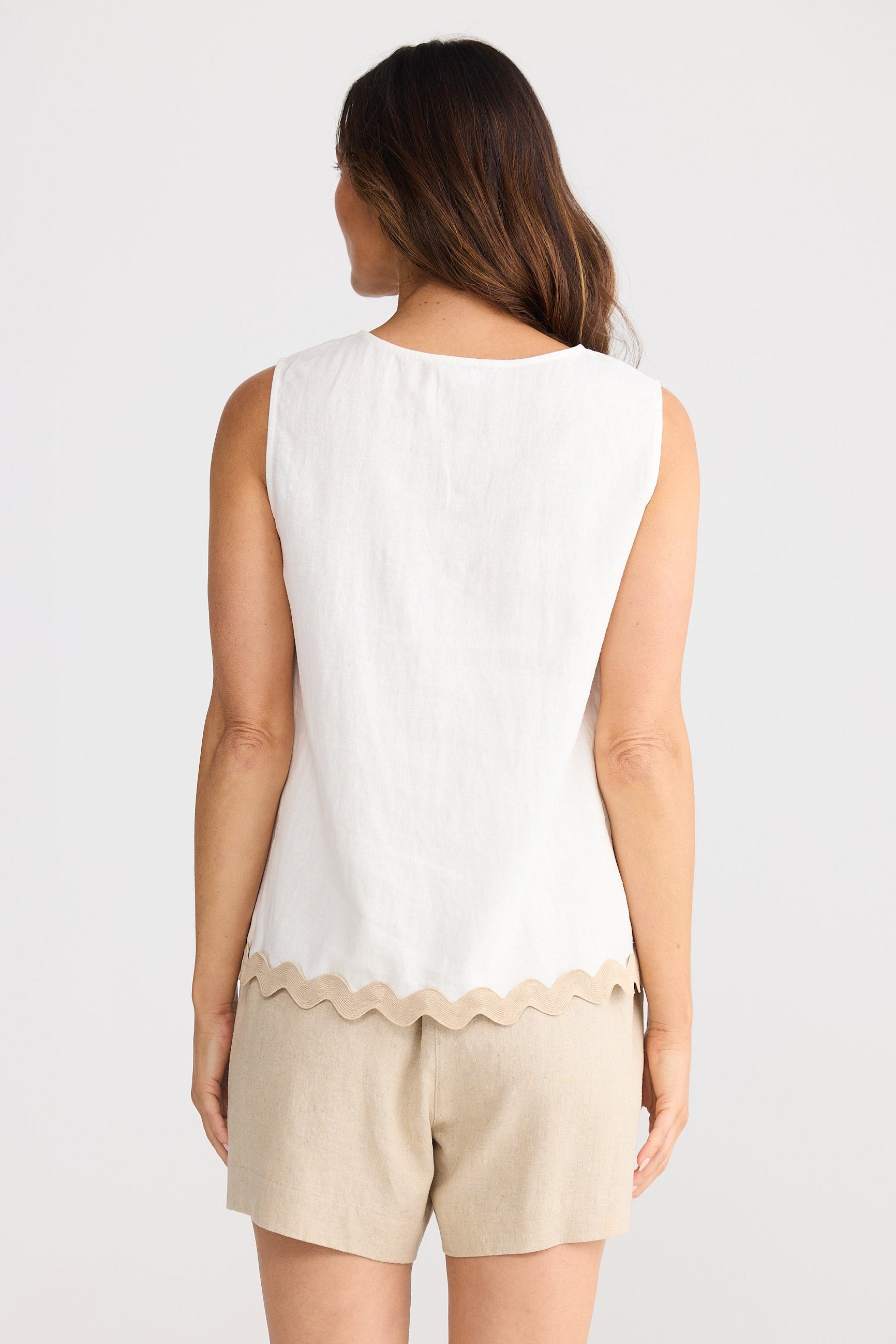 Woman wearing a white sleeveless top and beige shorts on a plain background