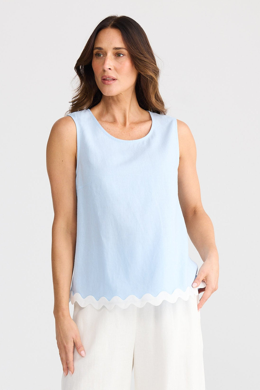 Woman wearing a light blue sleeveless top and white pants on a white background