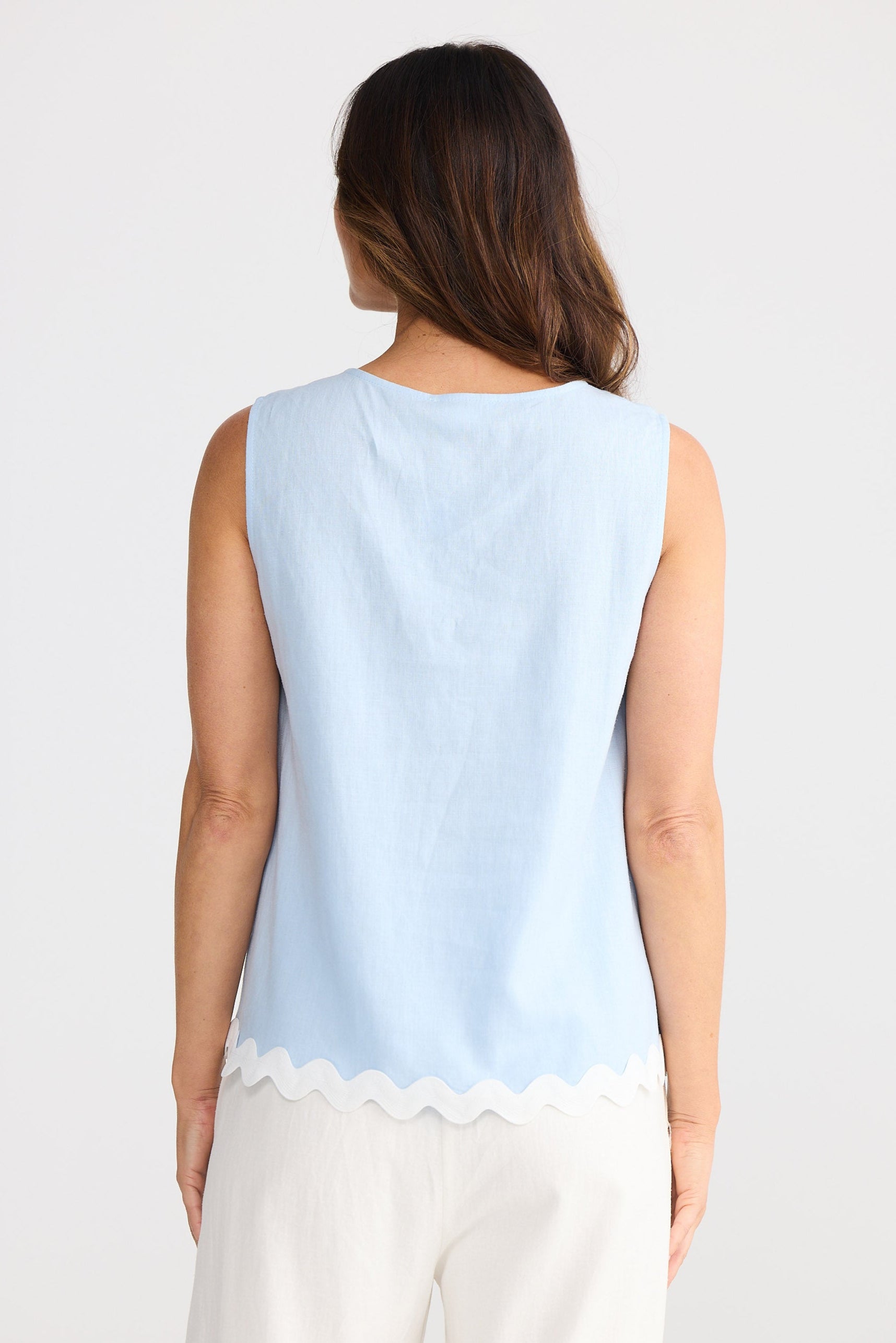 Woman wearing a light blue sleeveless top with a scalloped hem on a white background