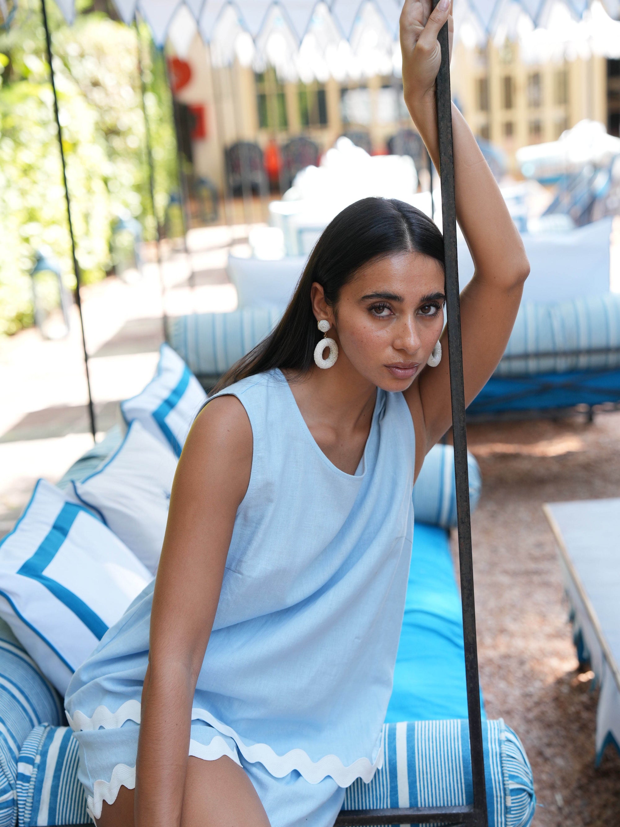 Woman in a light blue top and shorts sitting on a blue cushioned chair outdoors.