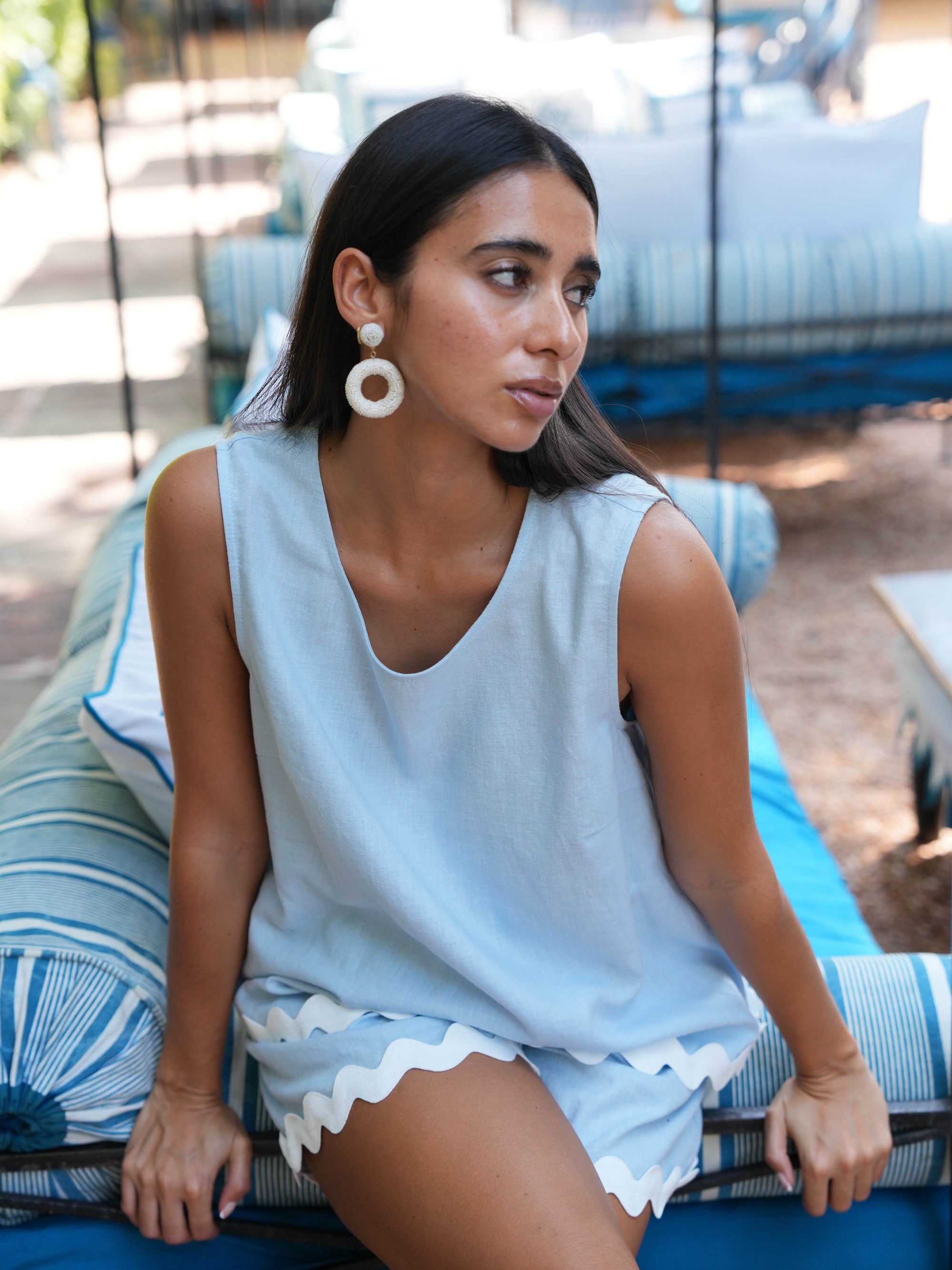 Woman in light blue sleeveless top and shorts sitting on a striped chair outdoors.
