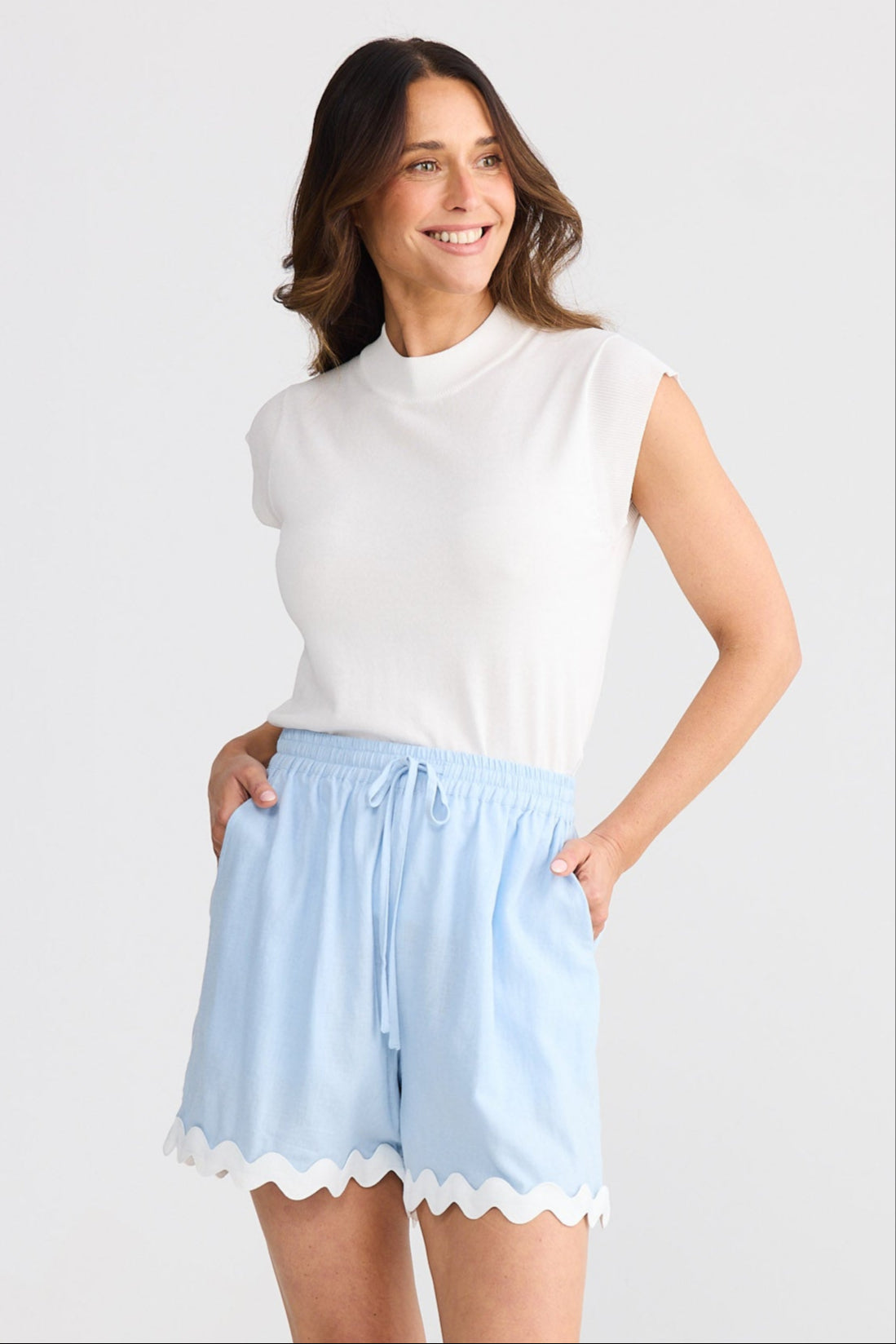 Woman wearing a white sleeveless top and light blue shorts on a white background