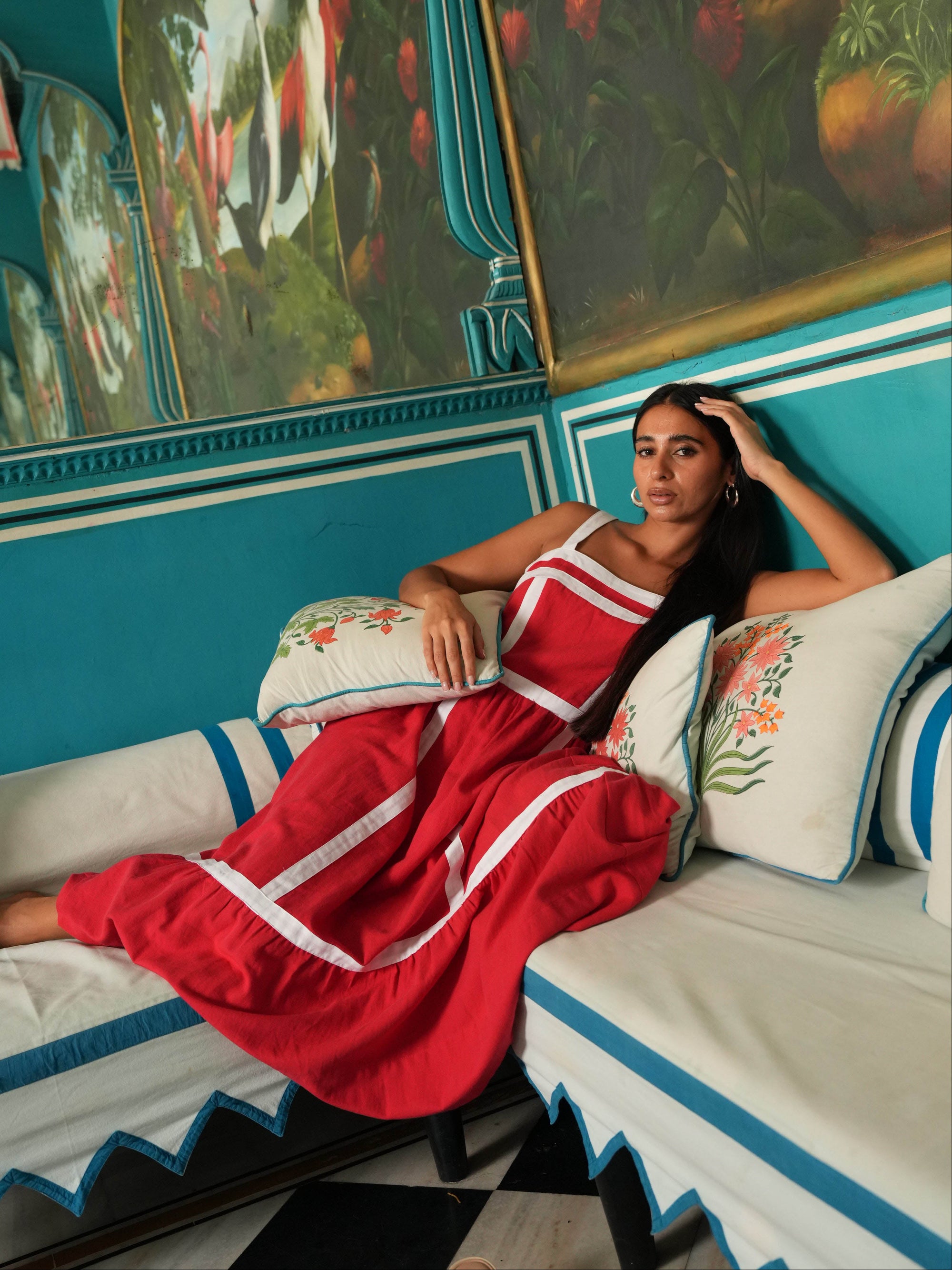 Woman in a red dress sitting on a couch with decorative pillows and colorful wall art.