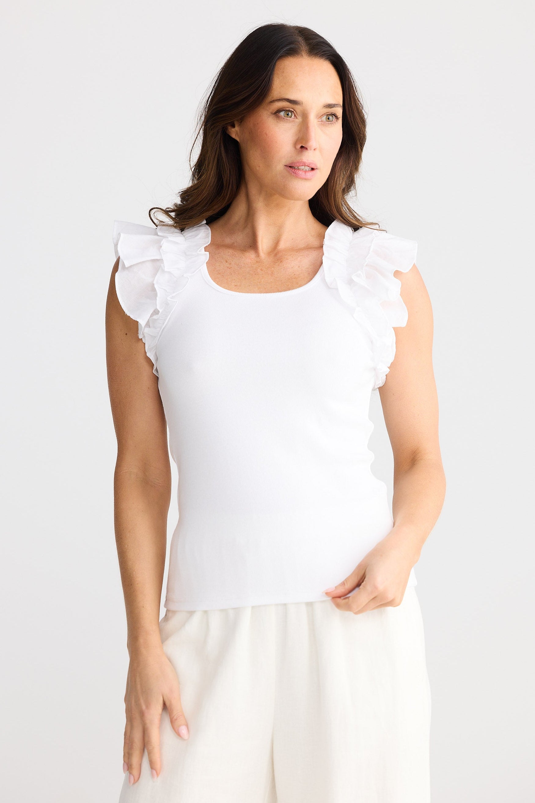 Woman wearing a white sleeveless top with ruffled shoulders against a plain background