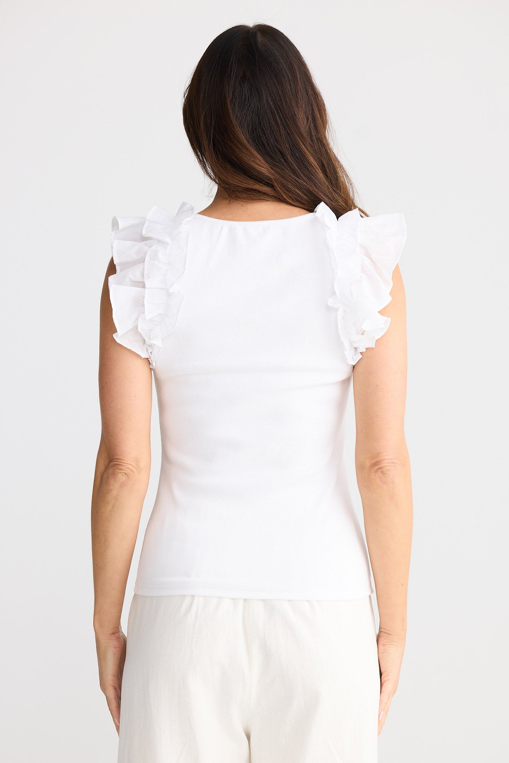 Woman wearing a white blouse with ruffled shoulders on a plain background