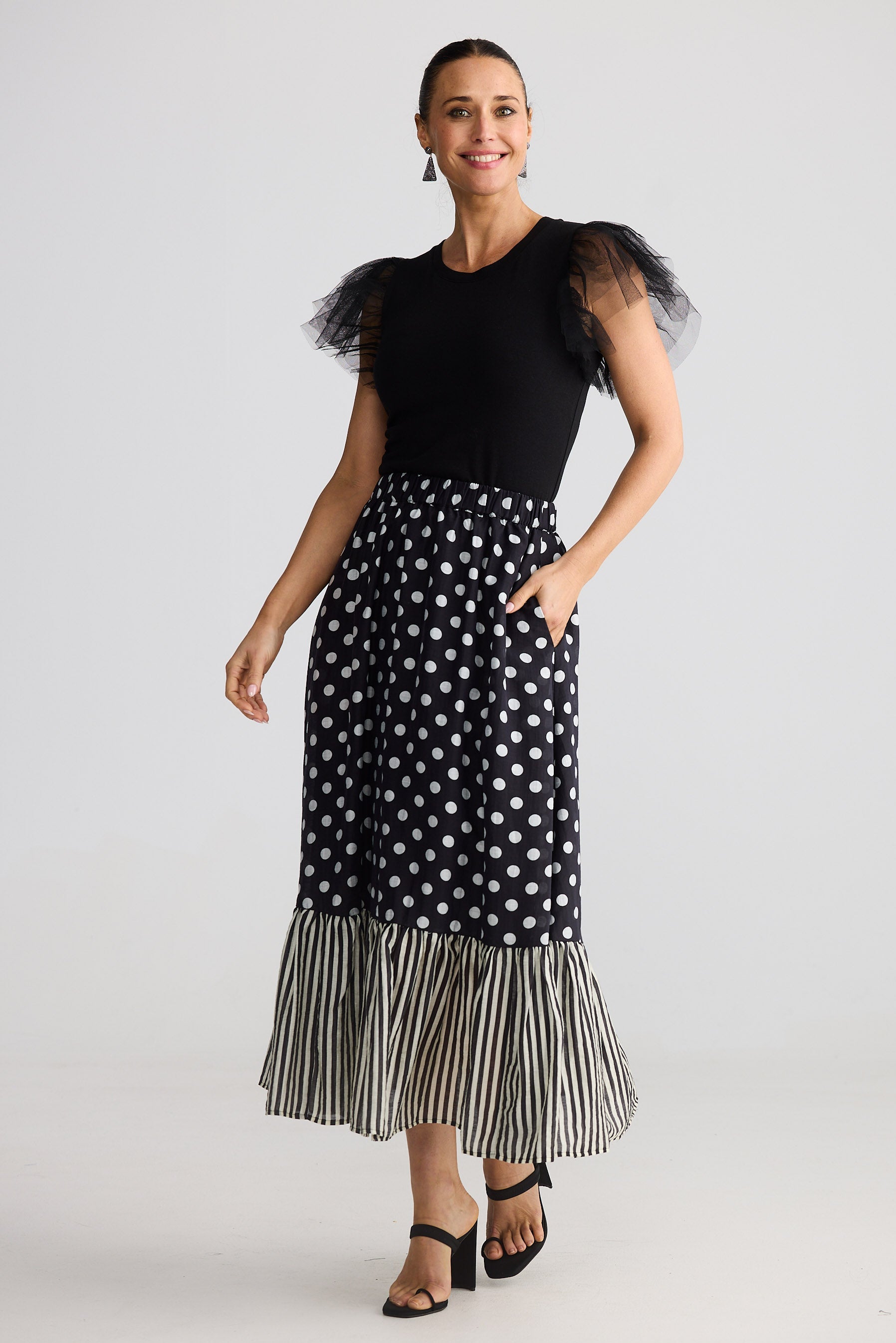 Woman wearing a black top with sheer sleeves and a polka dot skirt on a white background