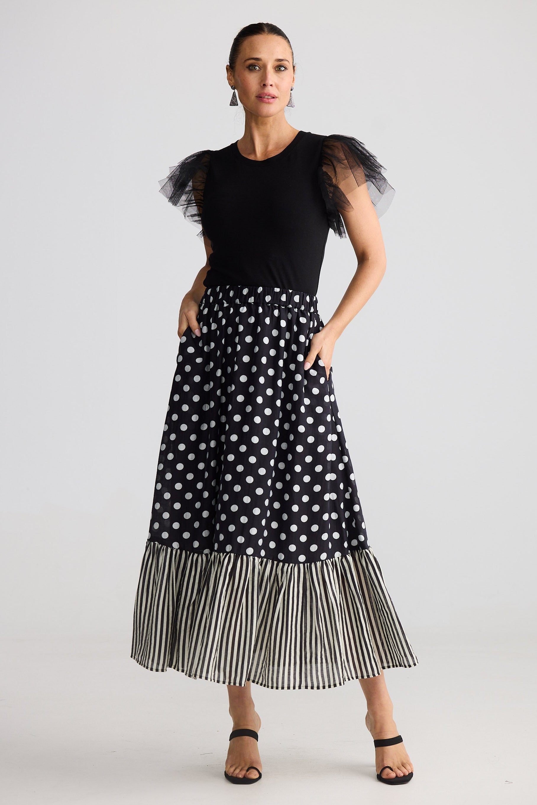 Woman wearing a black top with sheer sleeves and a polka dot skirt on a white background