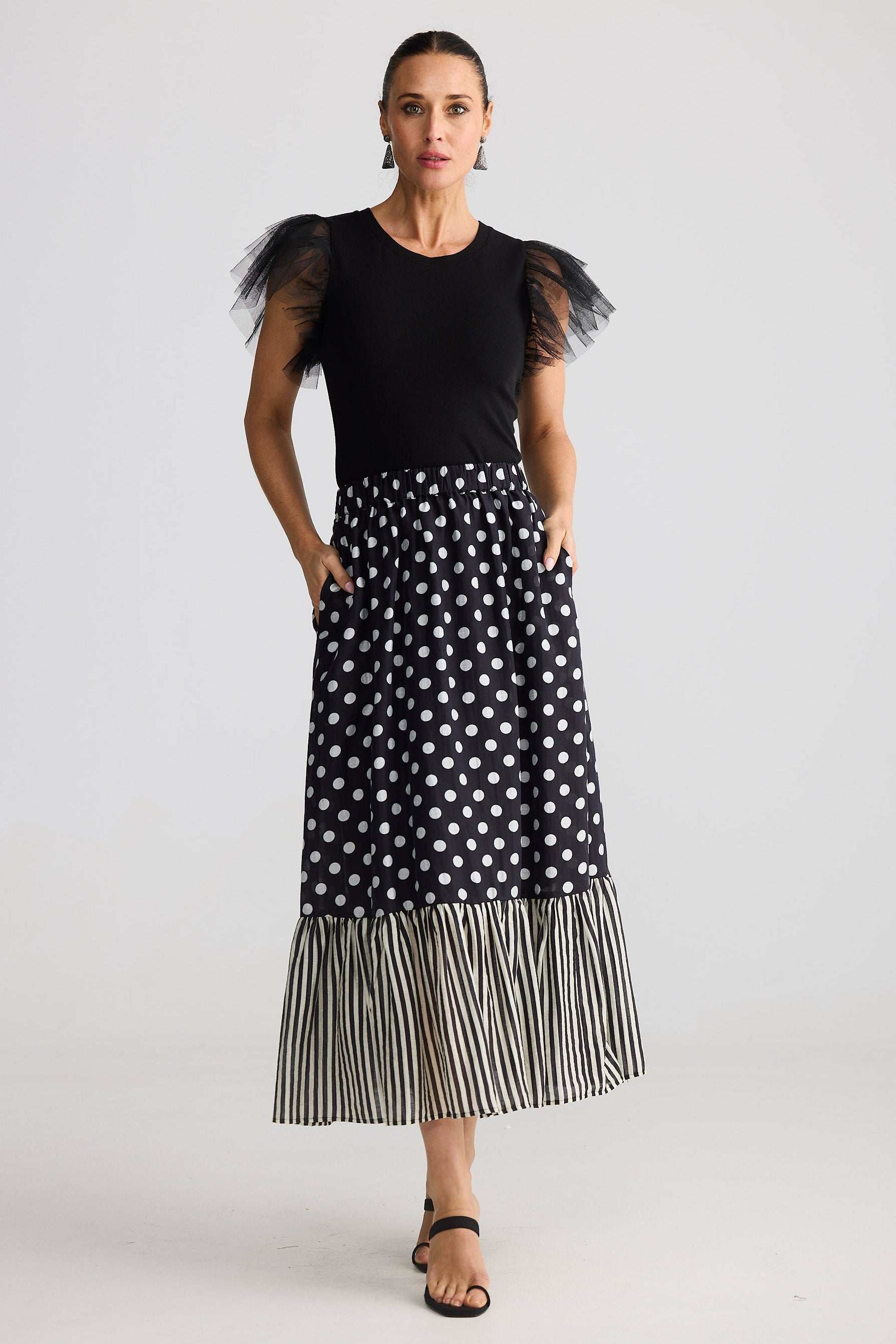 Woman wearing a black top with sheer sleeves and a black and white polka dot skirt on a white background