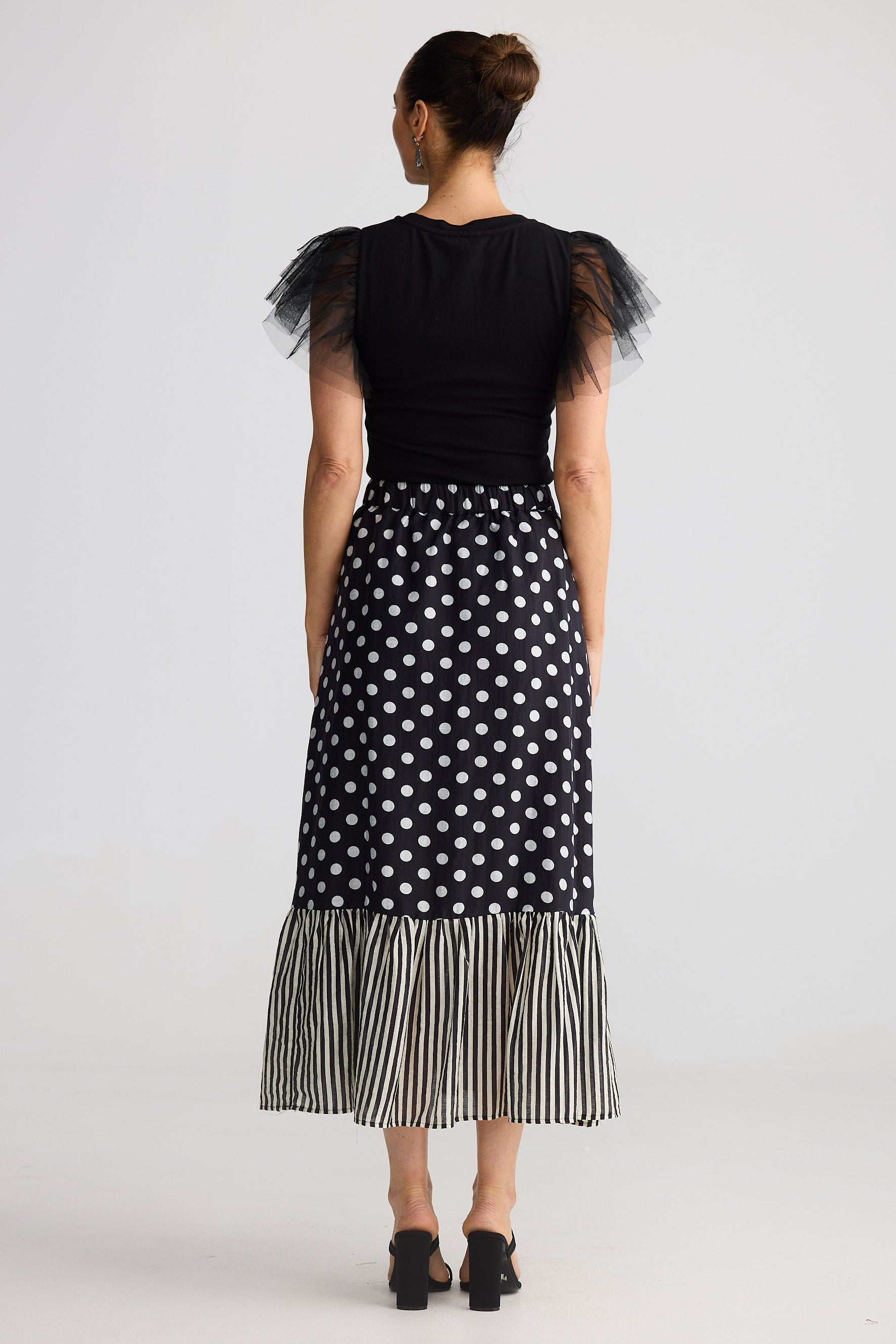 Woman wearing a black top with ruffled sleeves and a black and white polka dot skirt on a white background