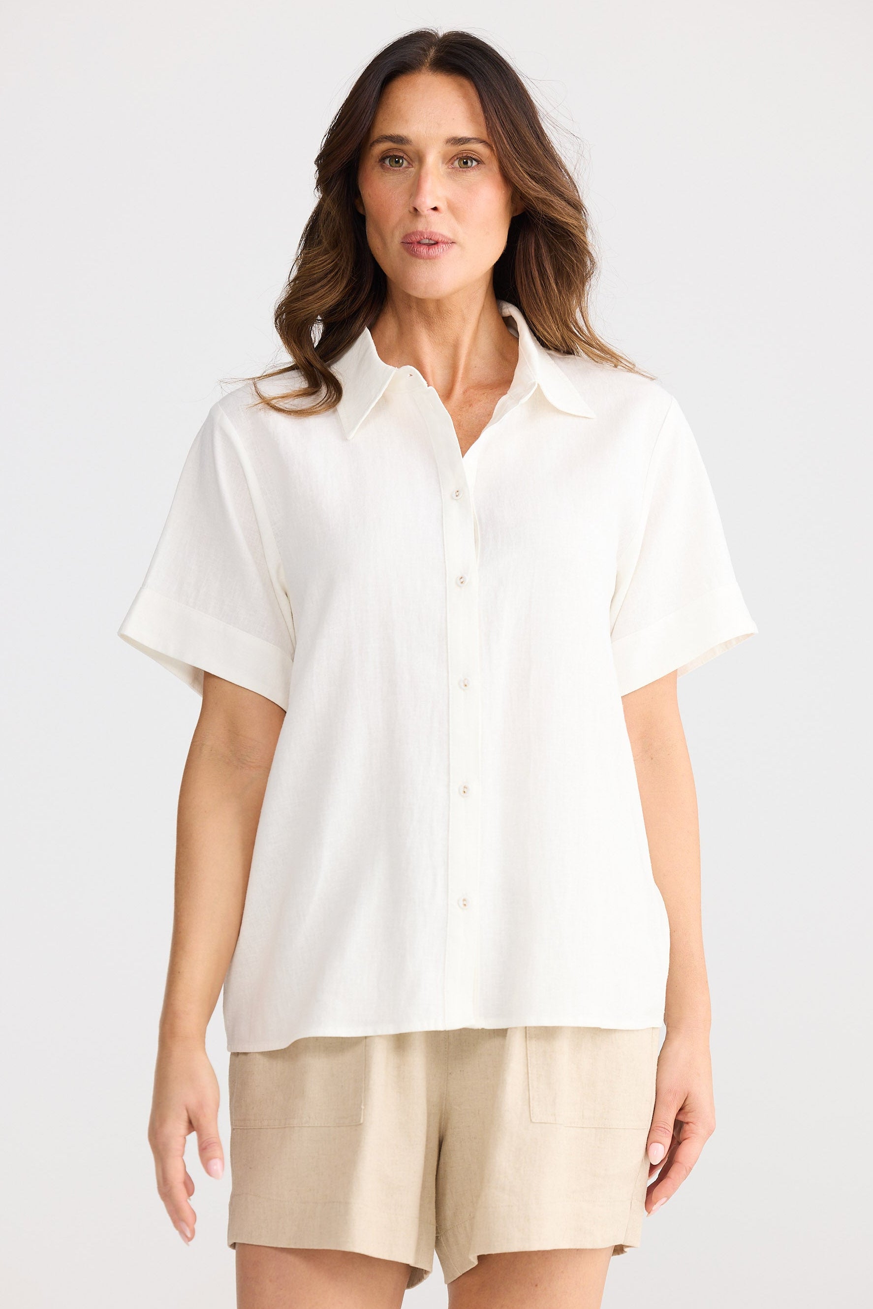 Woman wearing a white shirt and beige shorts on a plain background