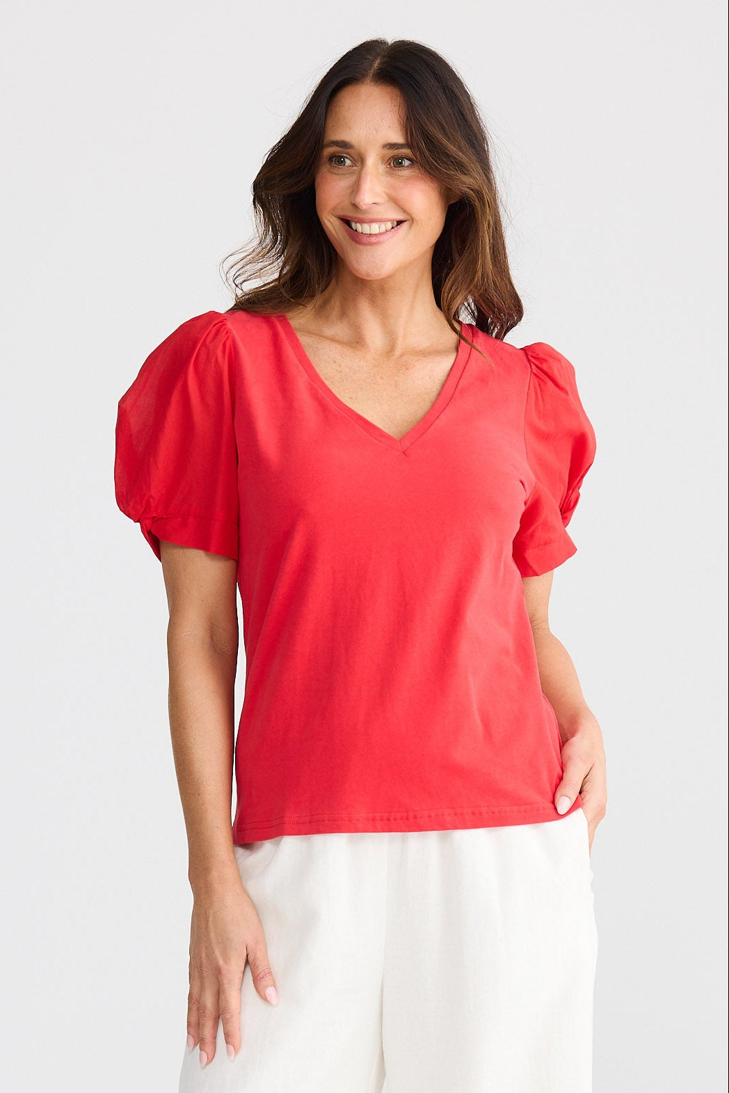 Woman wearing a red blouse and white pants on a white background