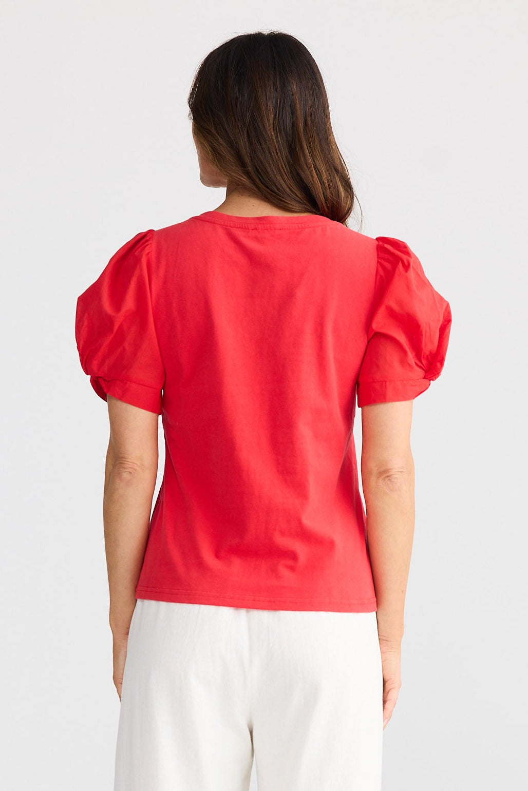 Woman wearing a red blouse and white pants on a light gray background