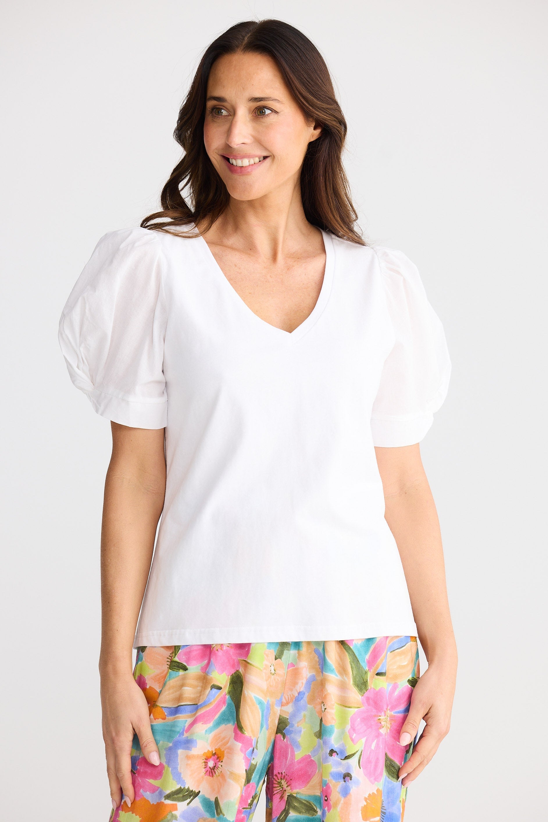 Woman wearing a white blouse and colorful floral pants on a white background