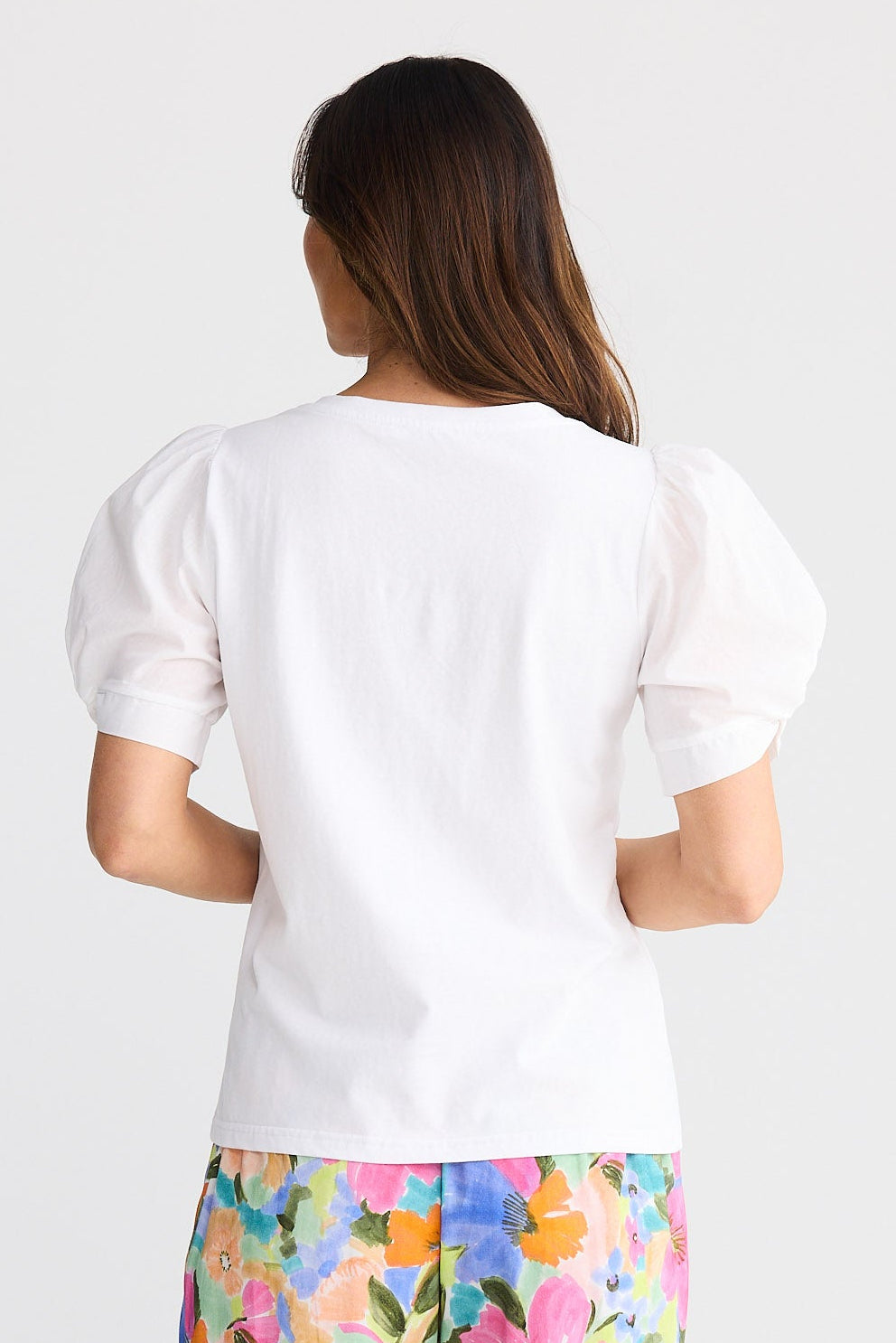 Person wearing a white top and colorful floral pants on a white background