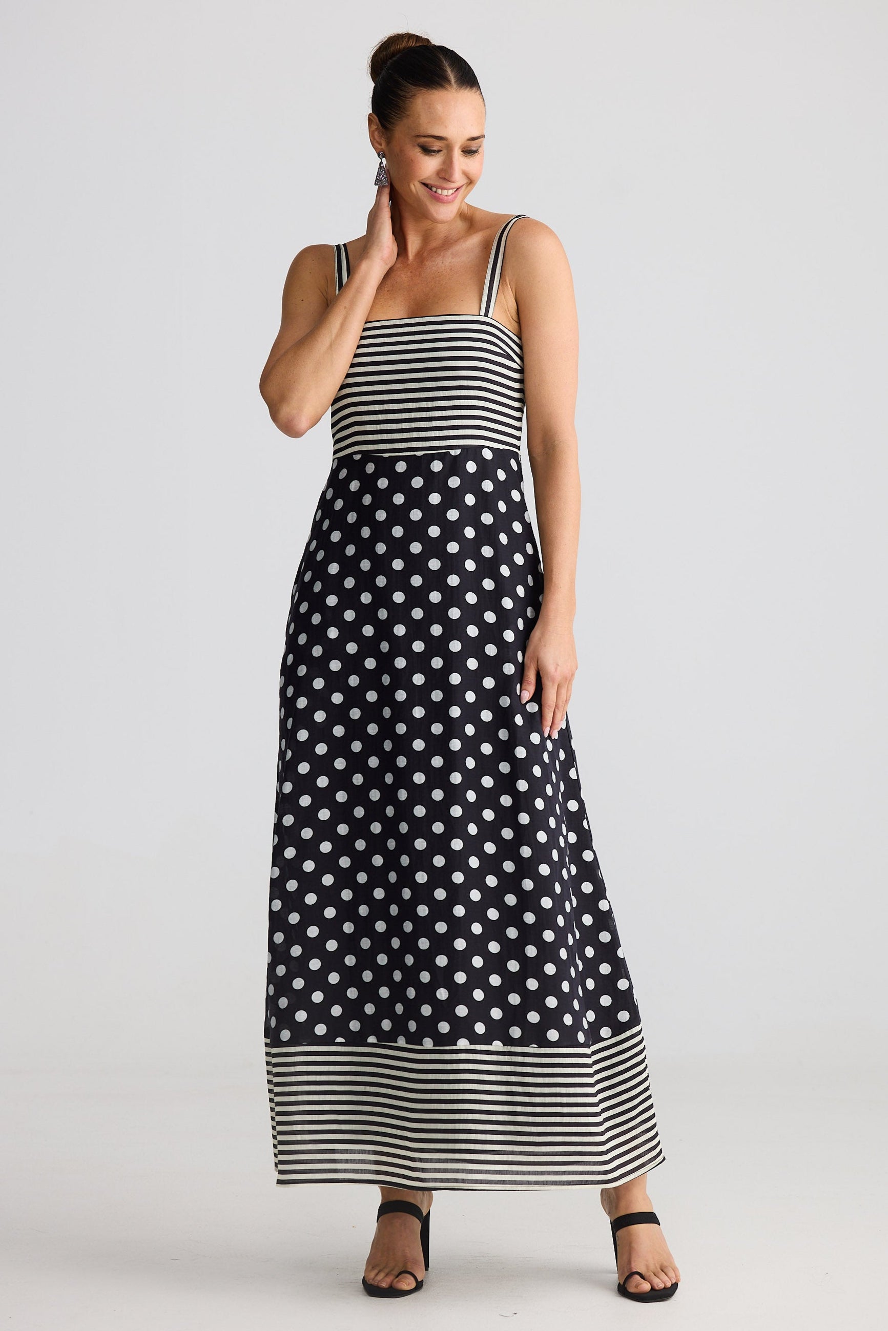 Woman wearing a black and white polka dot dress with a striped top on a light gray background