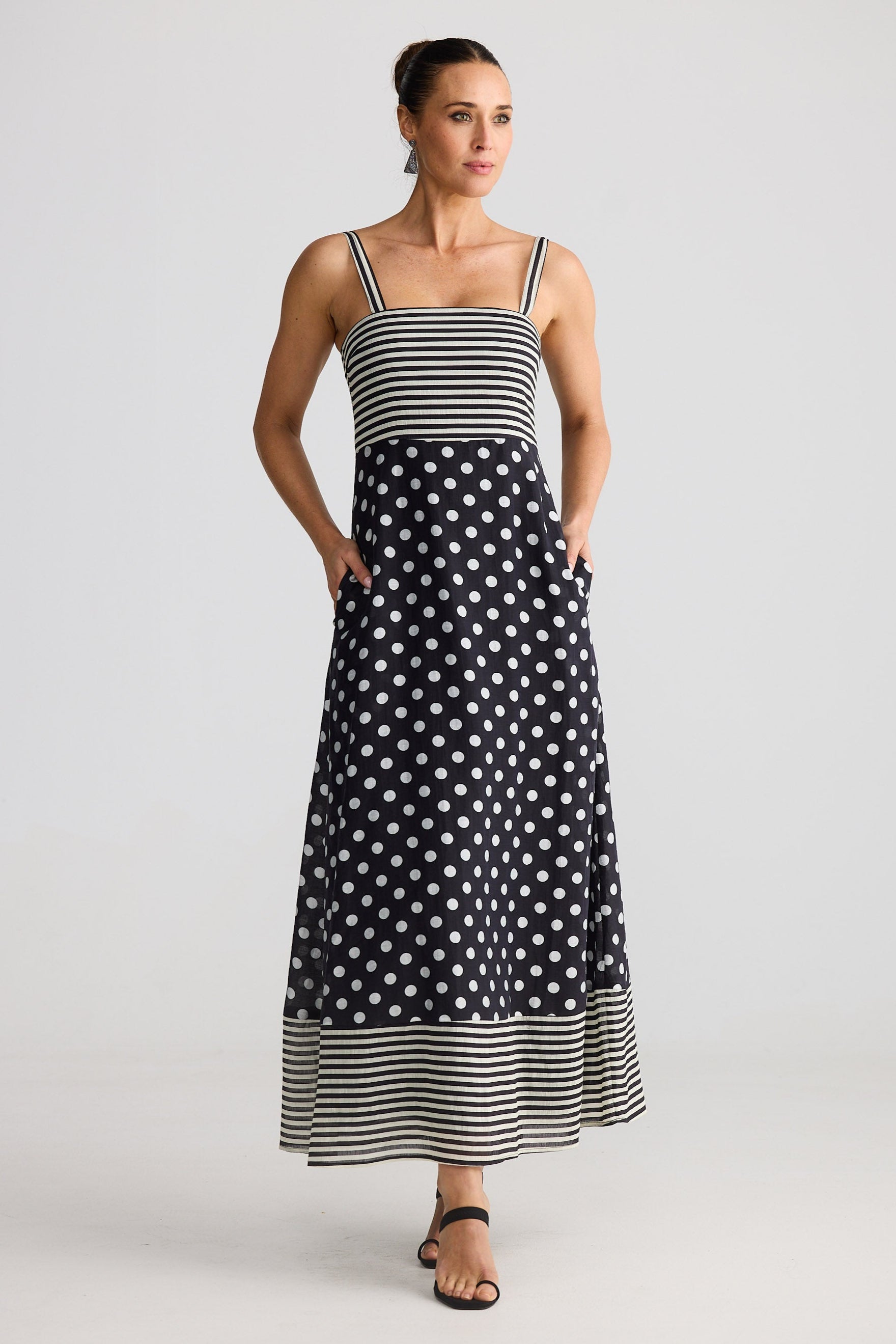 Woman wearing a black and white polka dot dress with a striped top on a plain background
