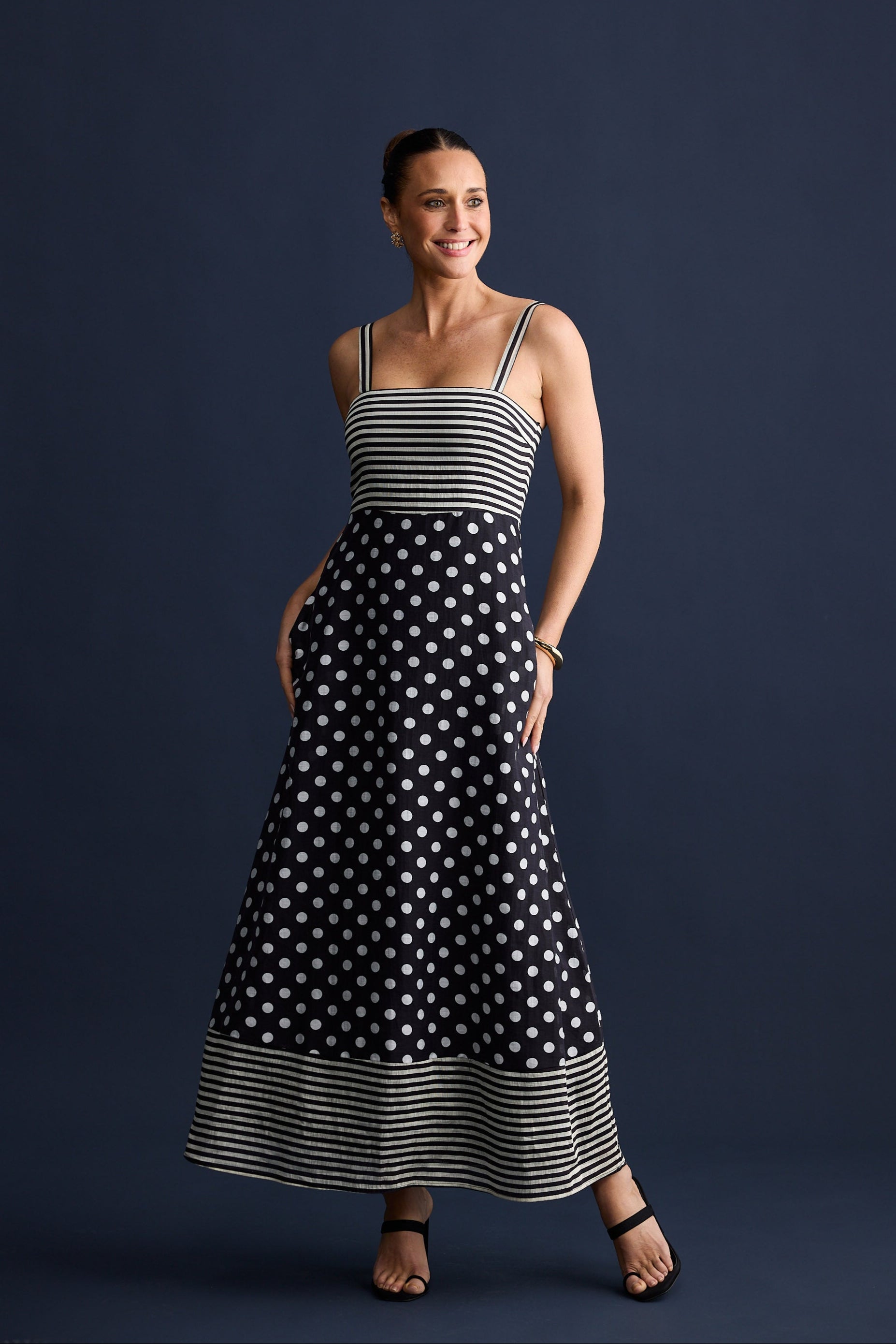 Woman wearing a black and white polka dot dress with a striped top against a dark background