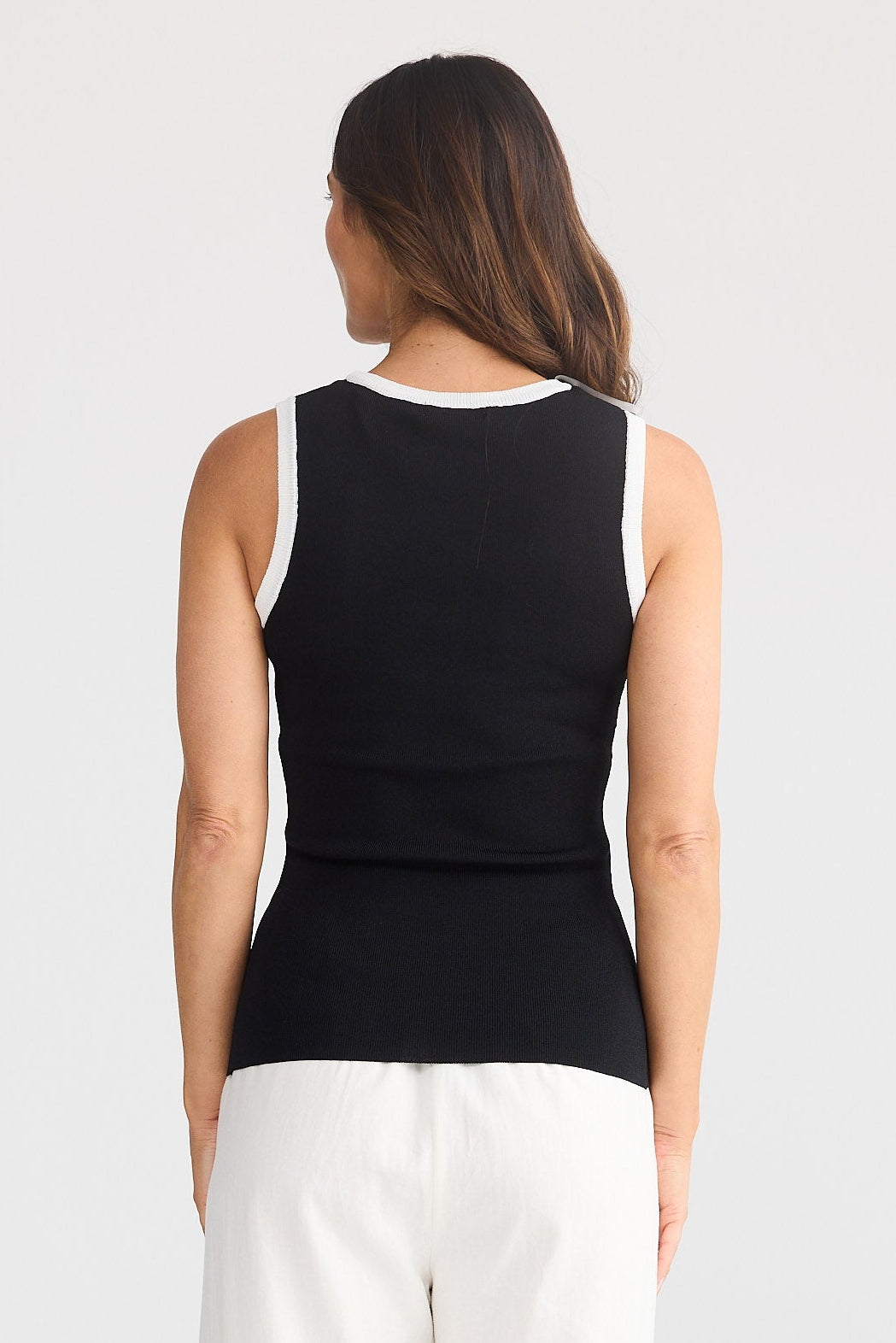 Woman wearing a black sleeveless top and white pants on a light gray background