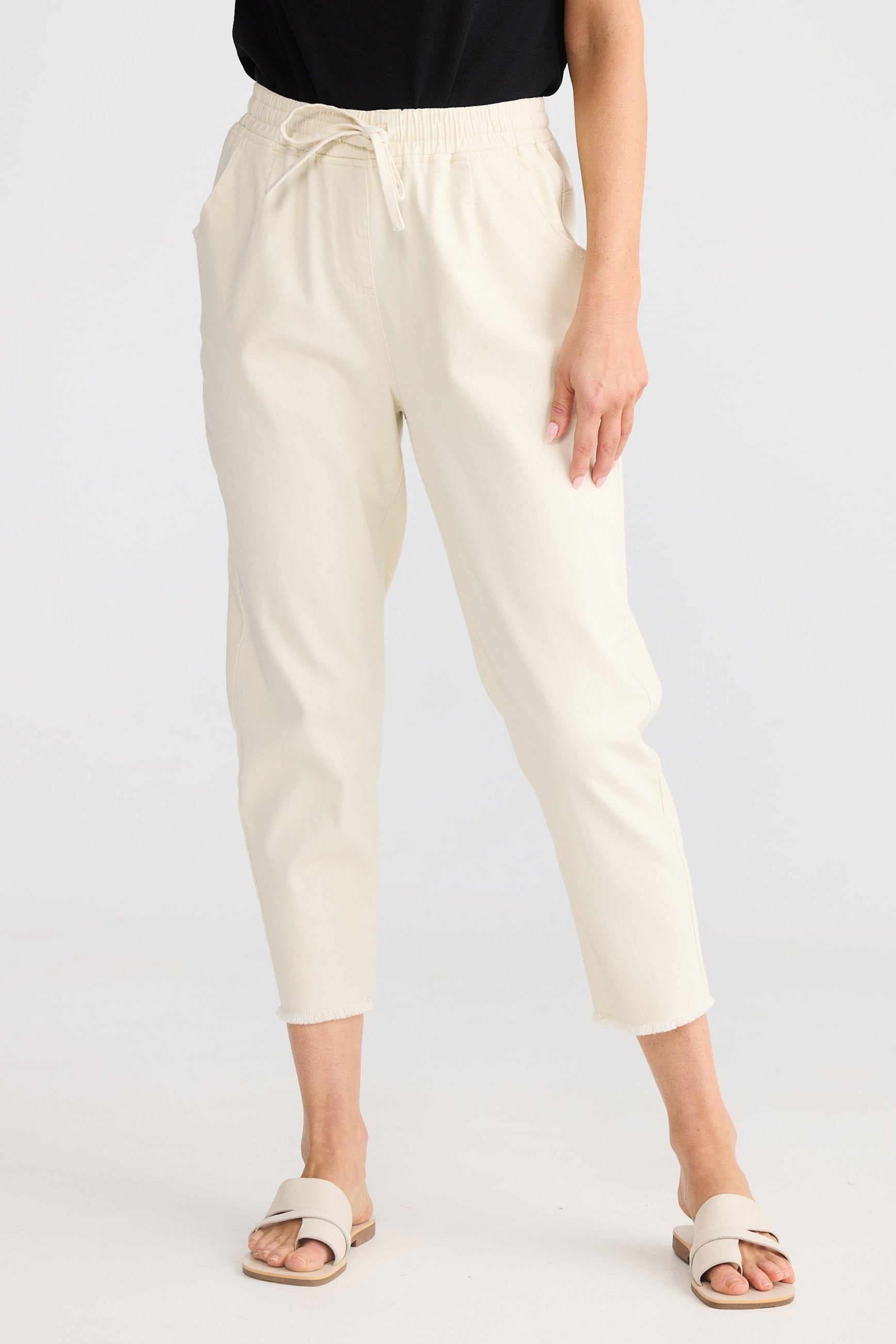 Woman wearing a black sleeveless top and beige pants on a white background