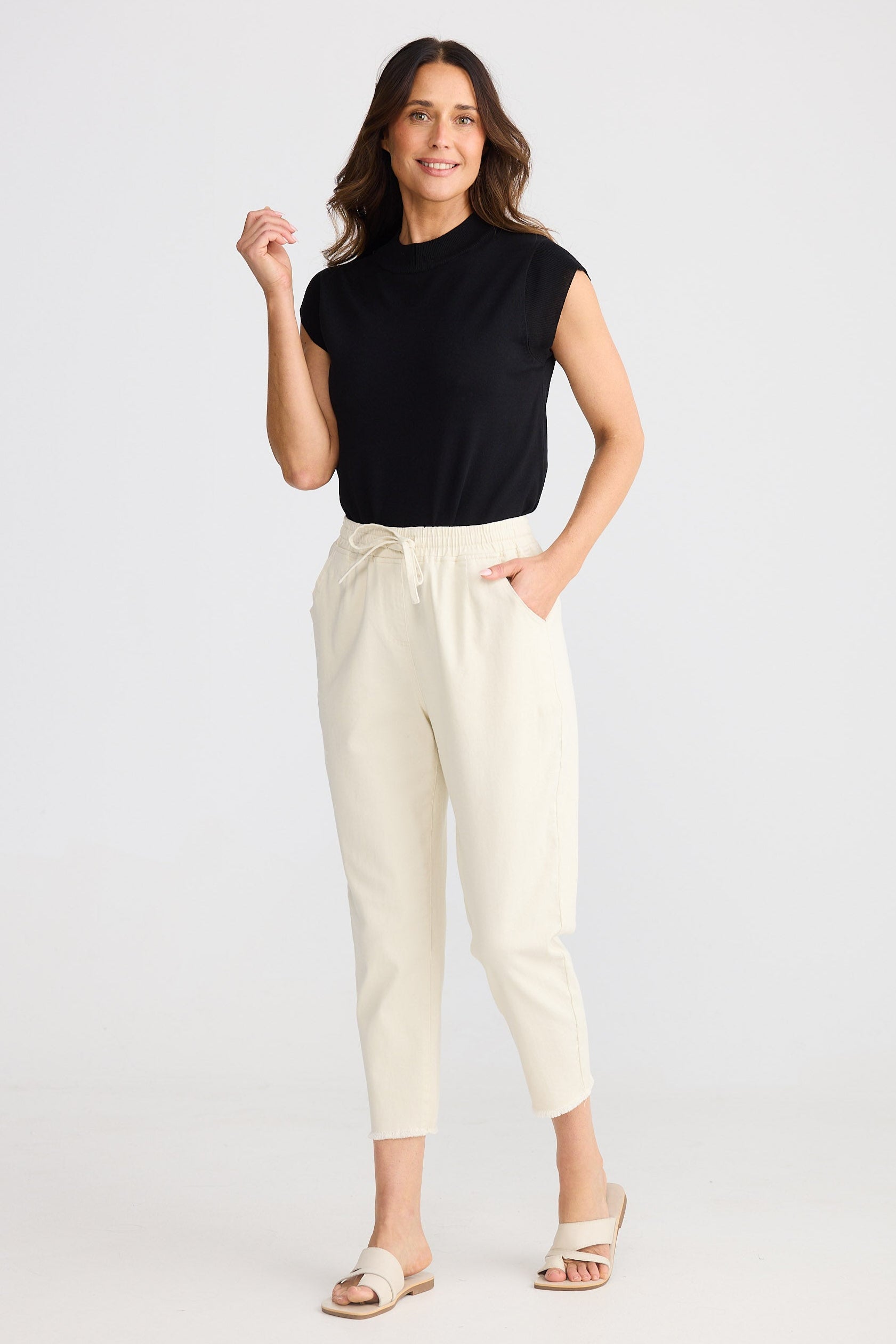 Woman wearing a black sleeveless top and beige pants on a white background