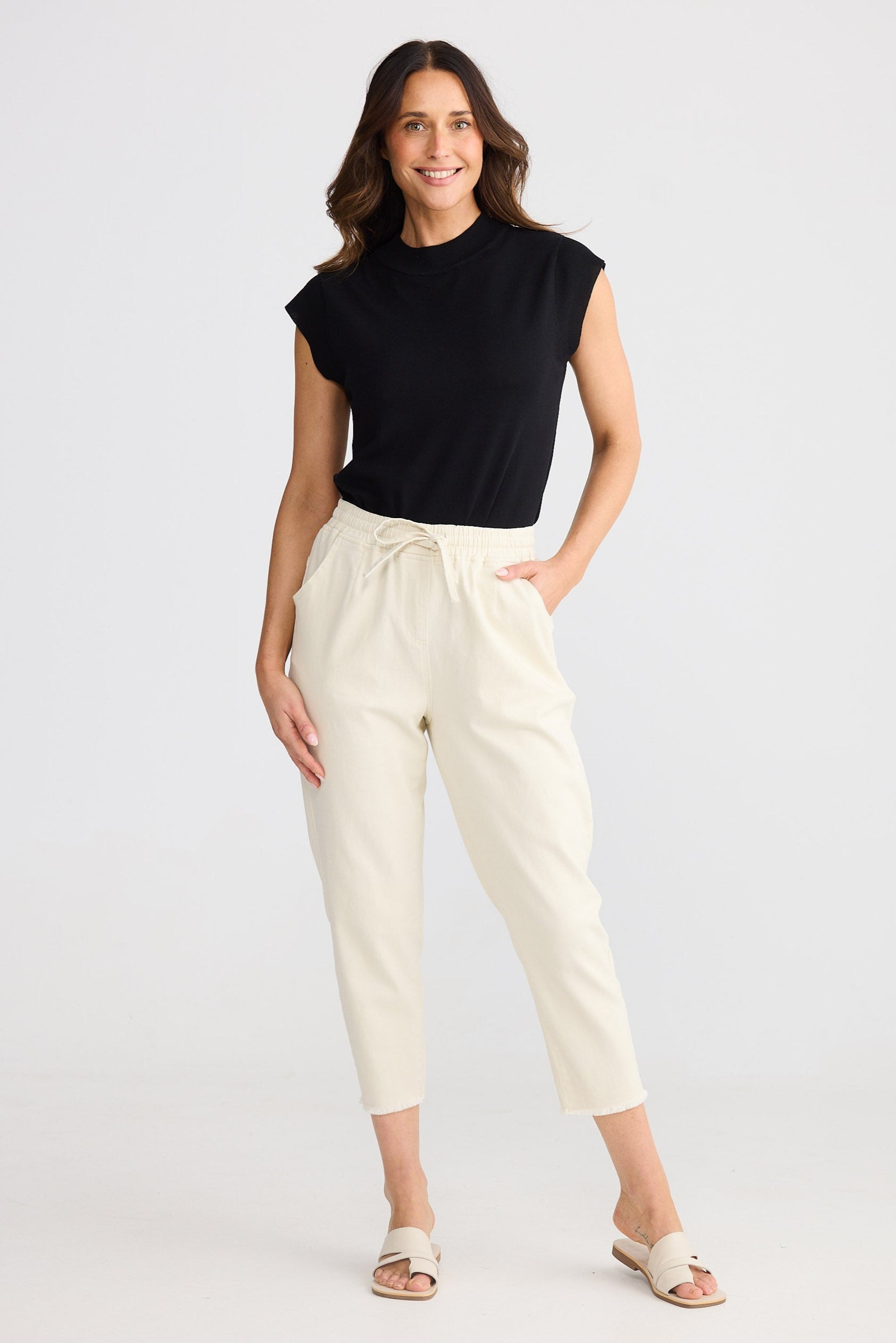 Woman wearing a black sleeveless top and beige pants on a white background