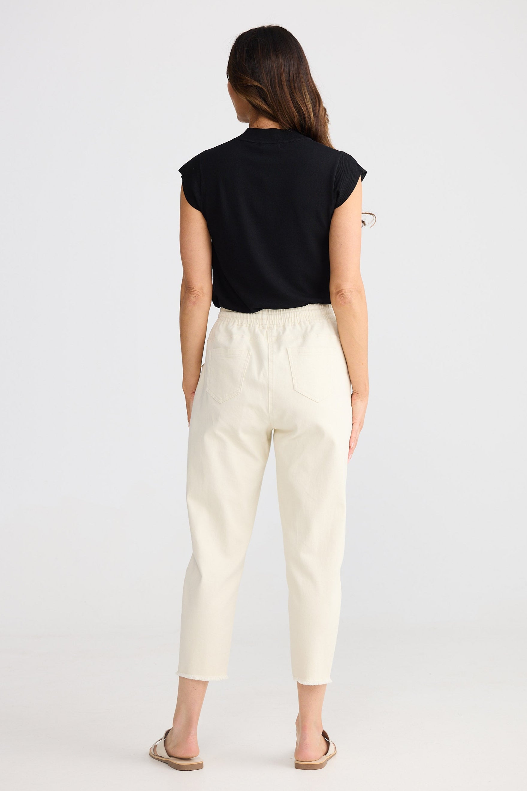 Woman wearing a black sleeveless top and beige pants on a white background