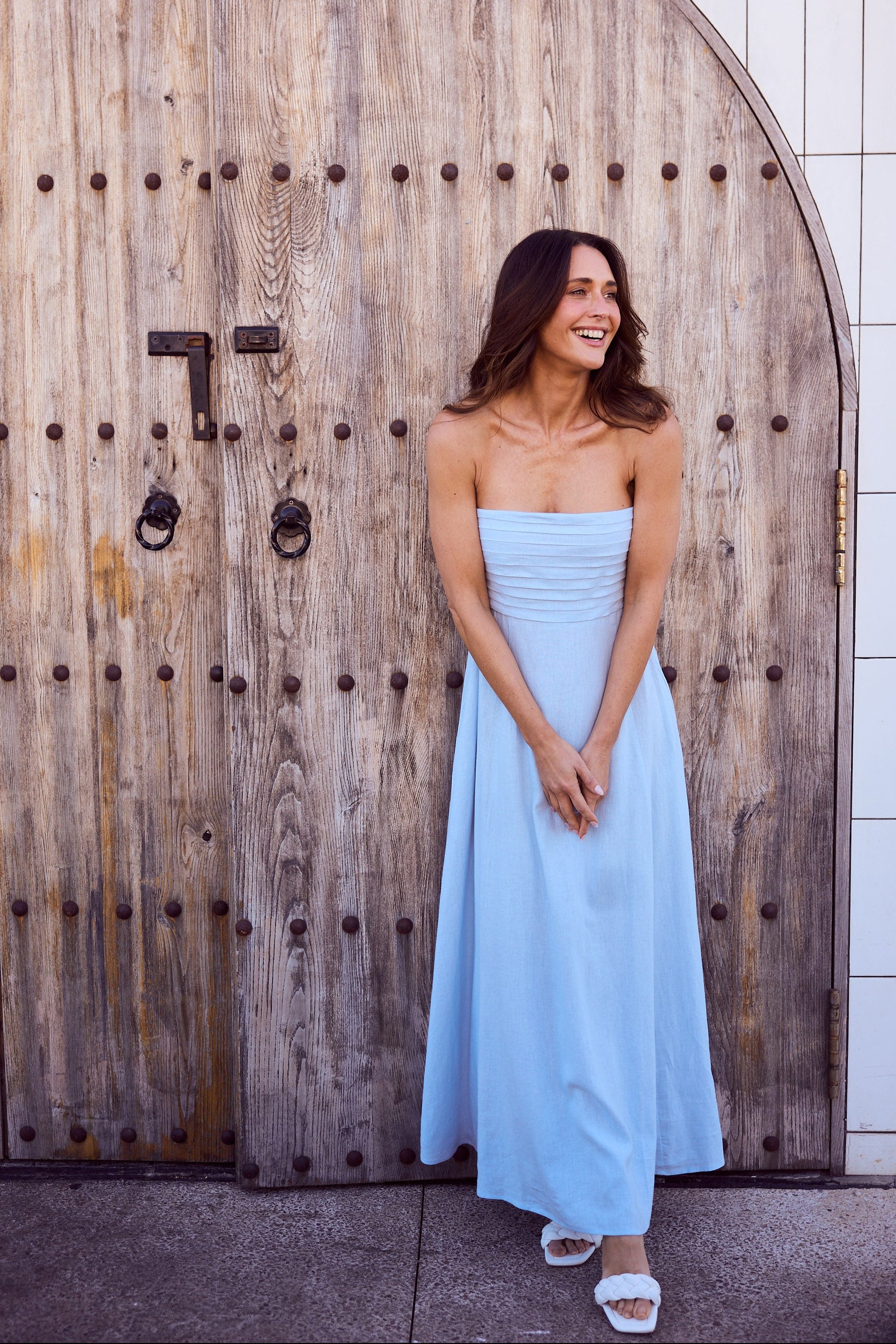 Woman in a light blue strapless dress standing in front of a wooden door.