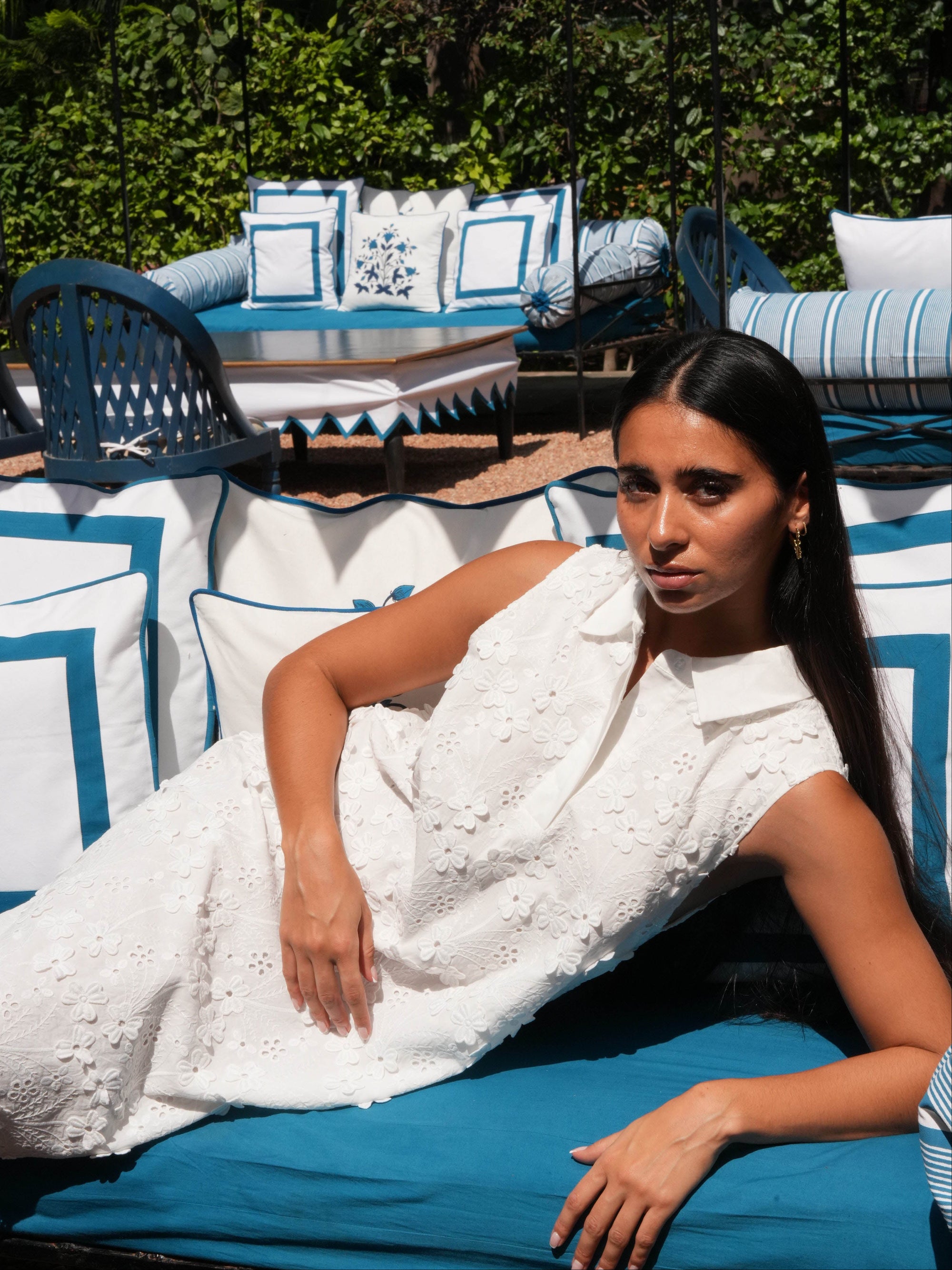 Woman in a white dress lying on a blue and white striped outdoor chair with greenery in the background