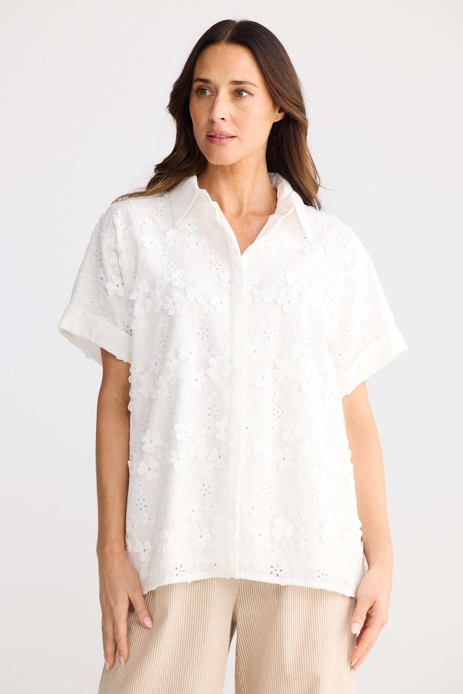 Woman wearing a white blouse with a subtle pattern on a plain background