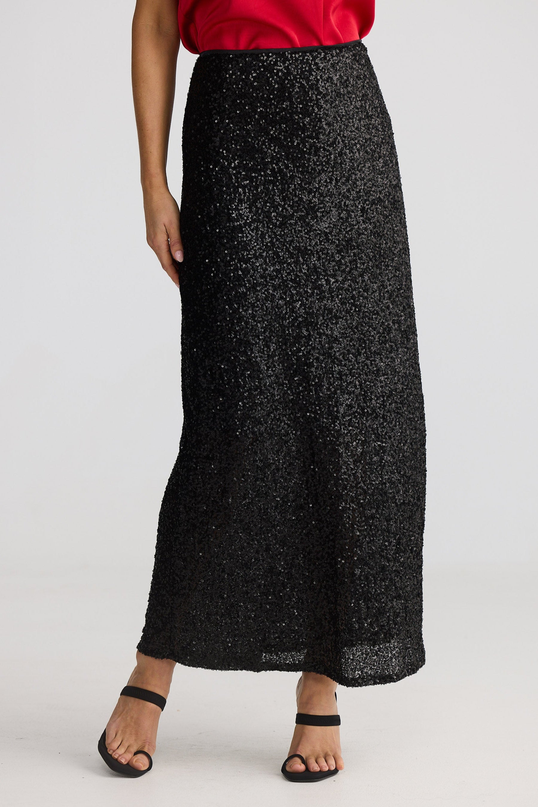 Woman wearing a red top and black sequin skirt on a white background