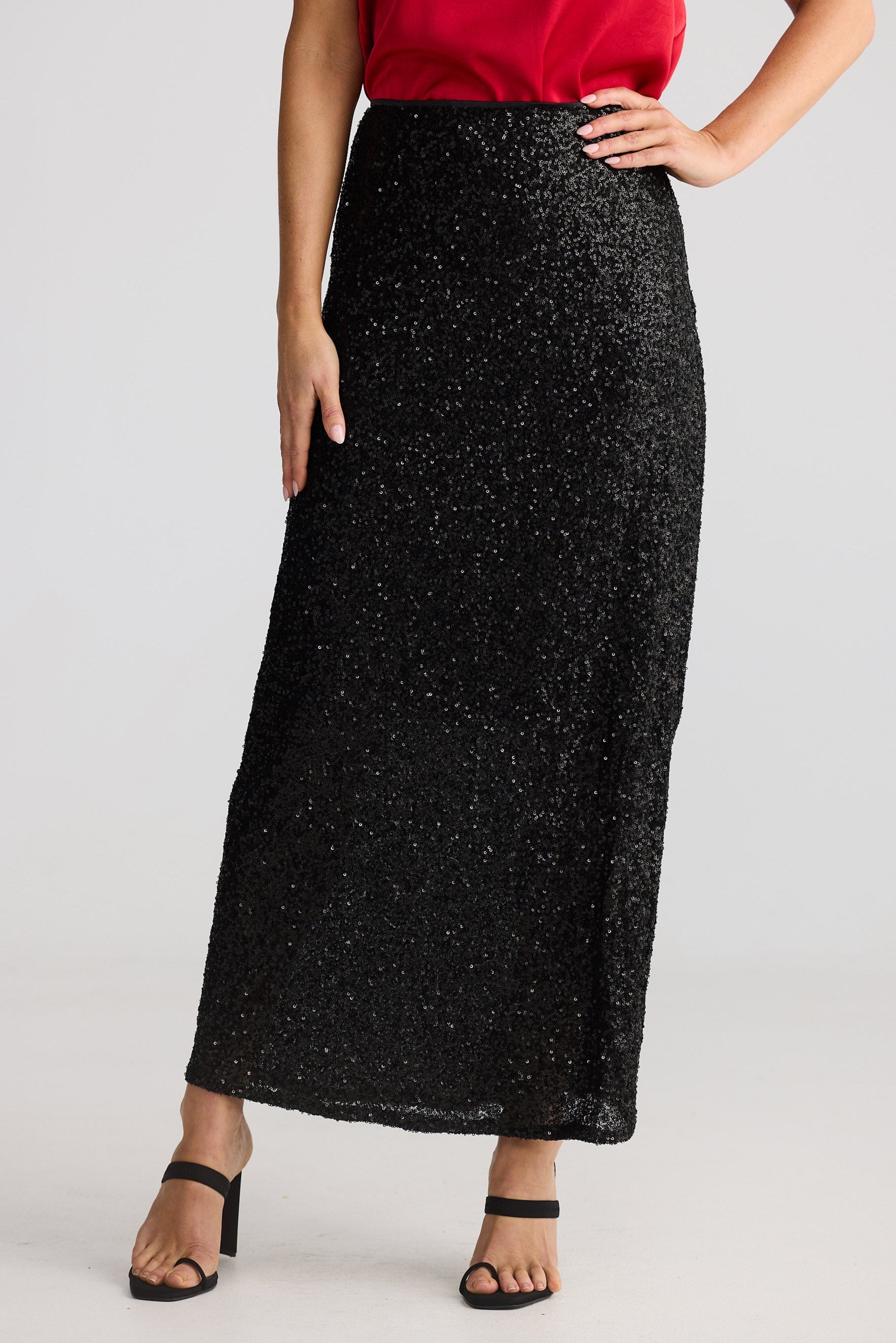 Person wearing a black sequin skirt and red top on a white background